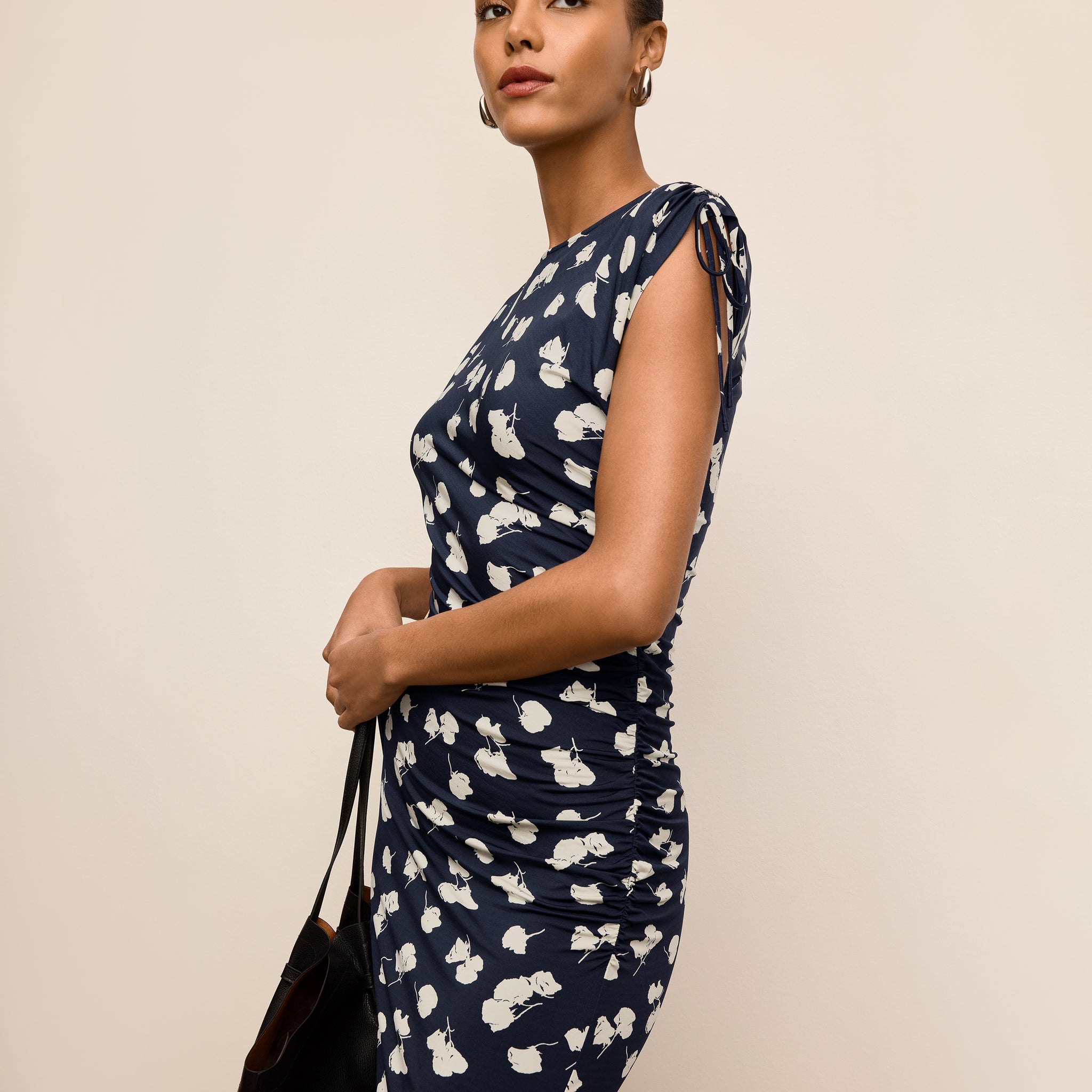 Woman wearing a navy dress with white floral pattern against a beige background