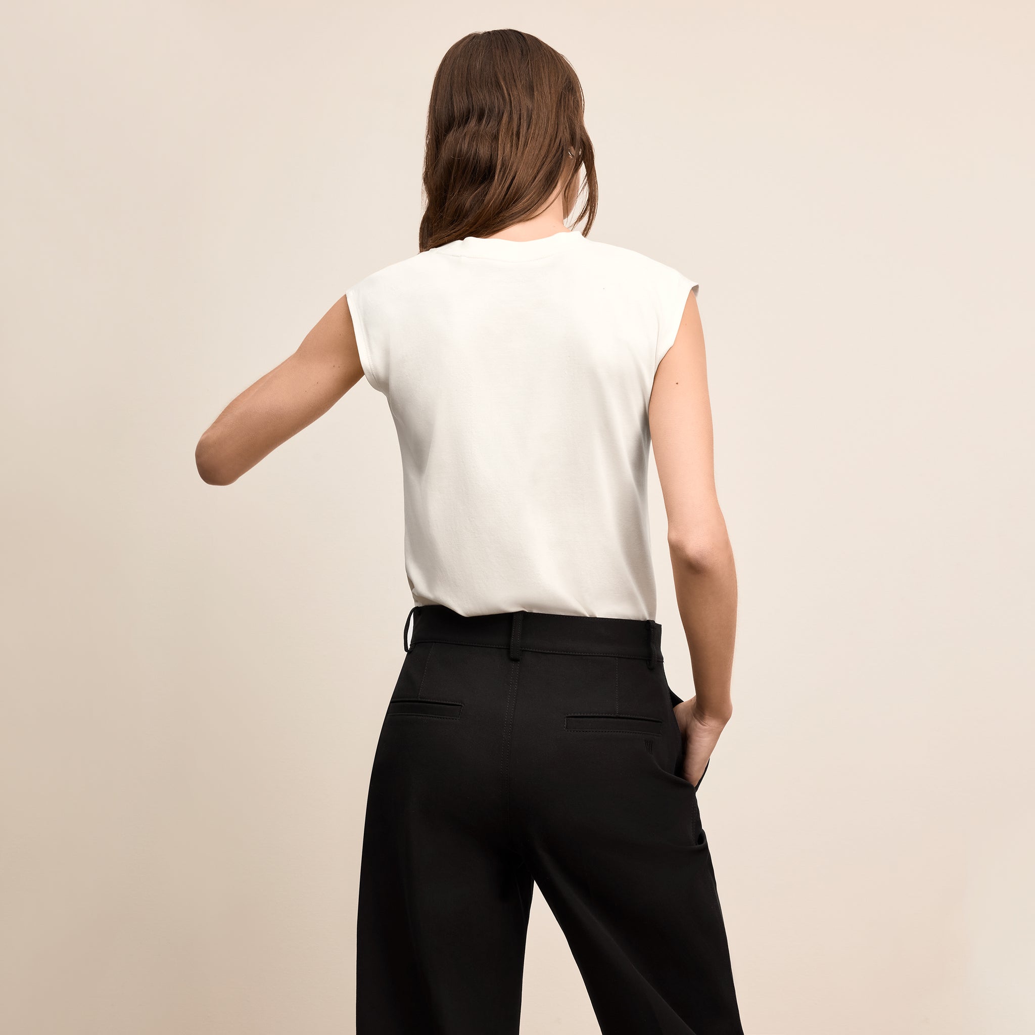 Woman wearing a white sleeveless top and black pants against a beige background
