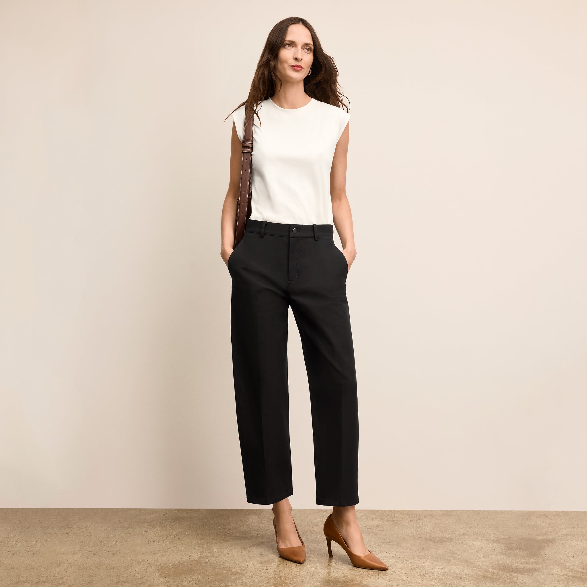 Woman wearing a white sleeveless top and black pants against a beige background 