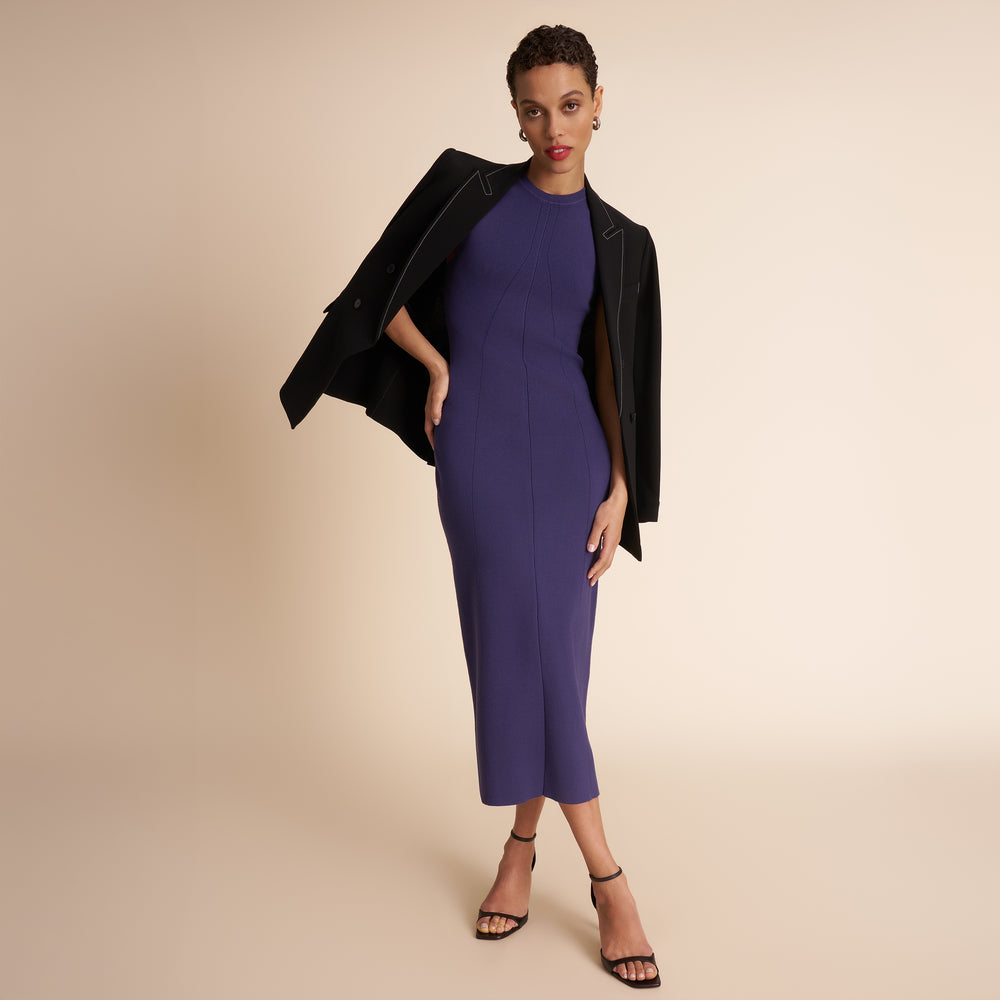 Woman wearing a purple dress with a black jacket on a beige background