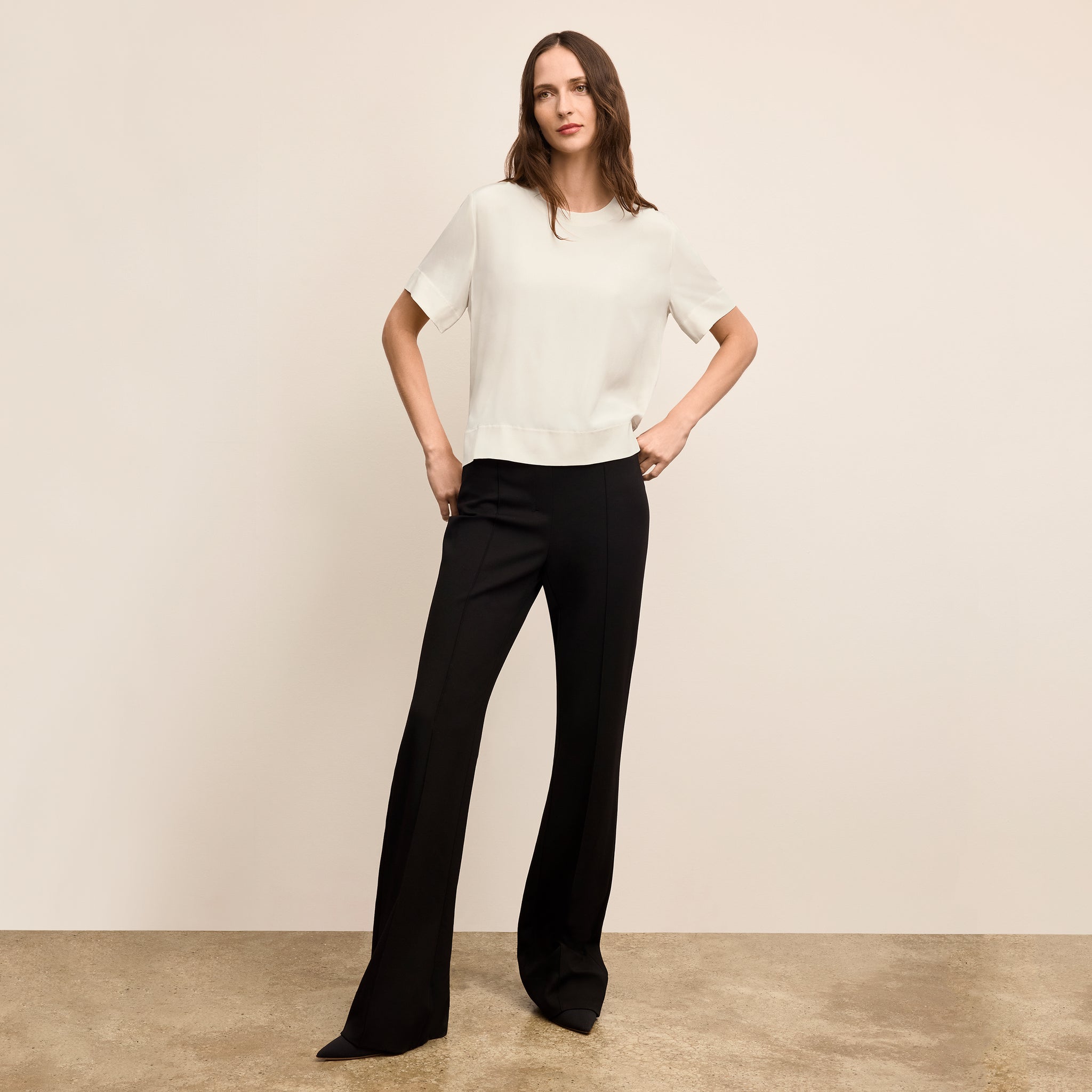 Woman wearing a white blouse and black pants against a beige background