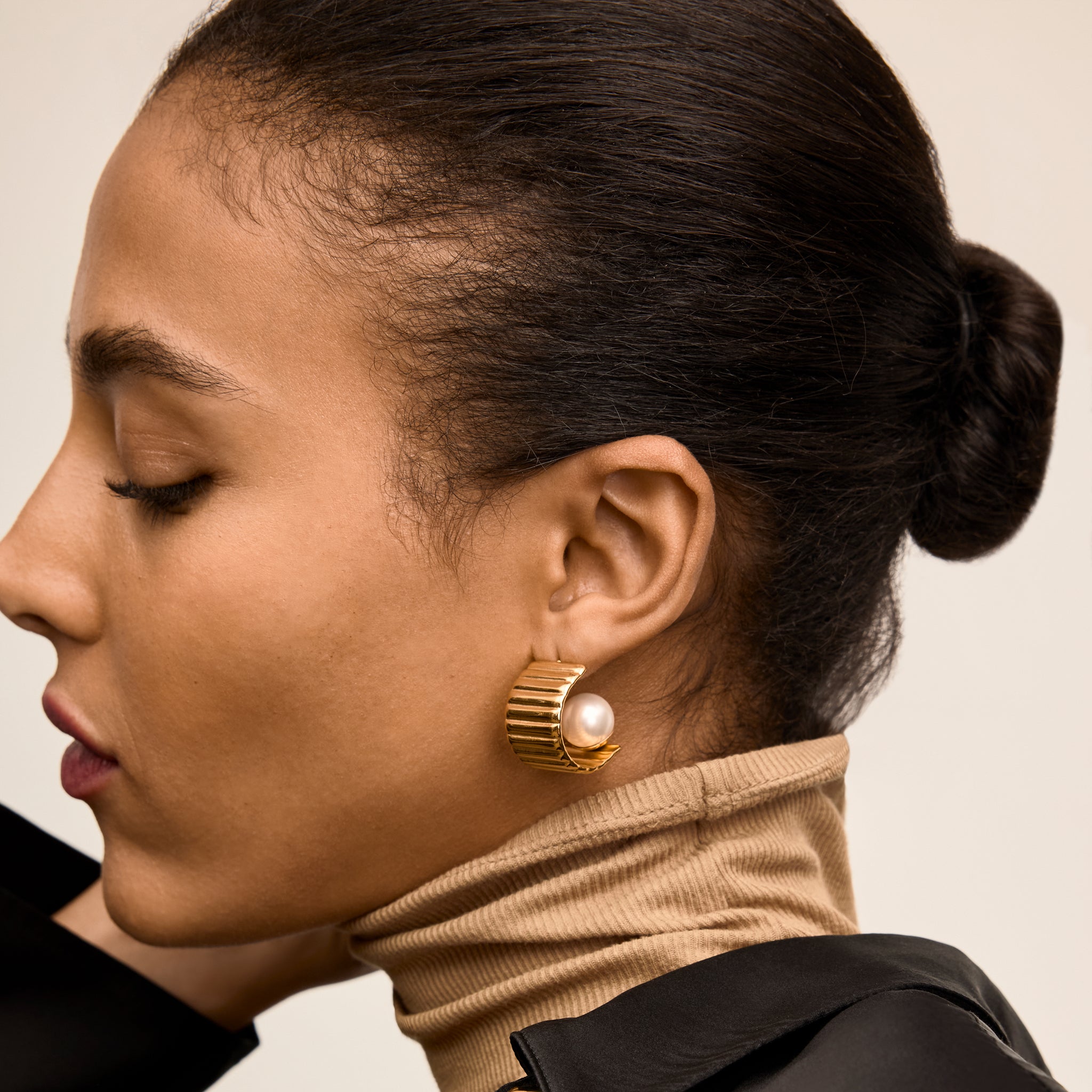 Close-up of a woman wearing gold hoop earrings with a pearl accent. 