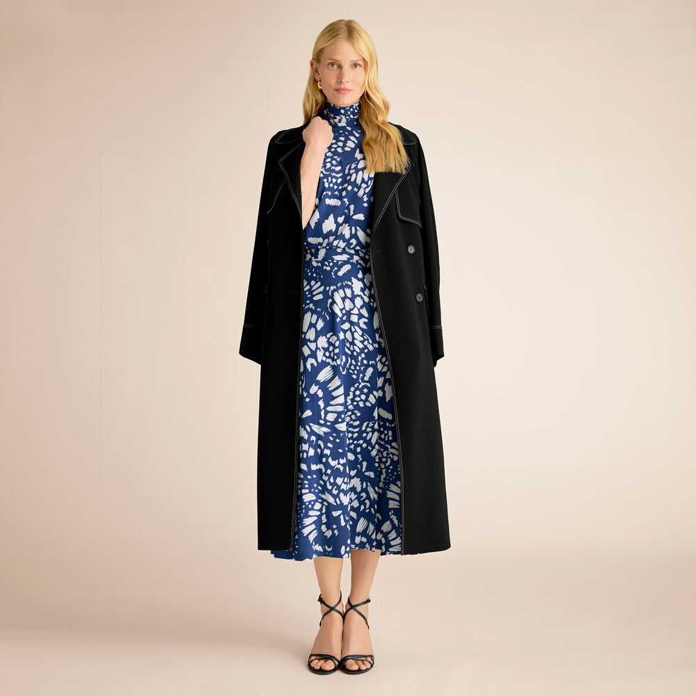 Woman wearing a blue floral dress with a black coat on a beige background