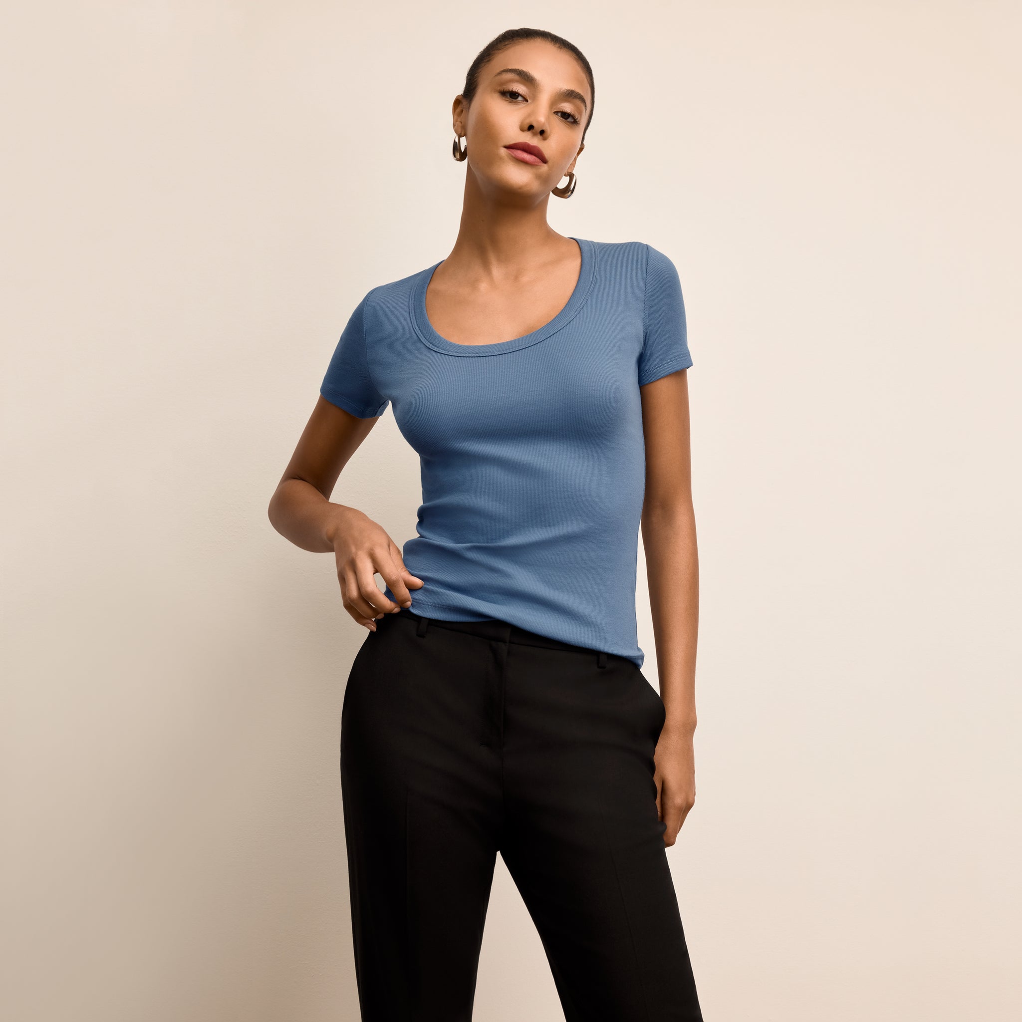 Woman wearing a blue t-shirt and black pants against a beige background 