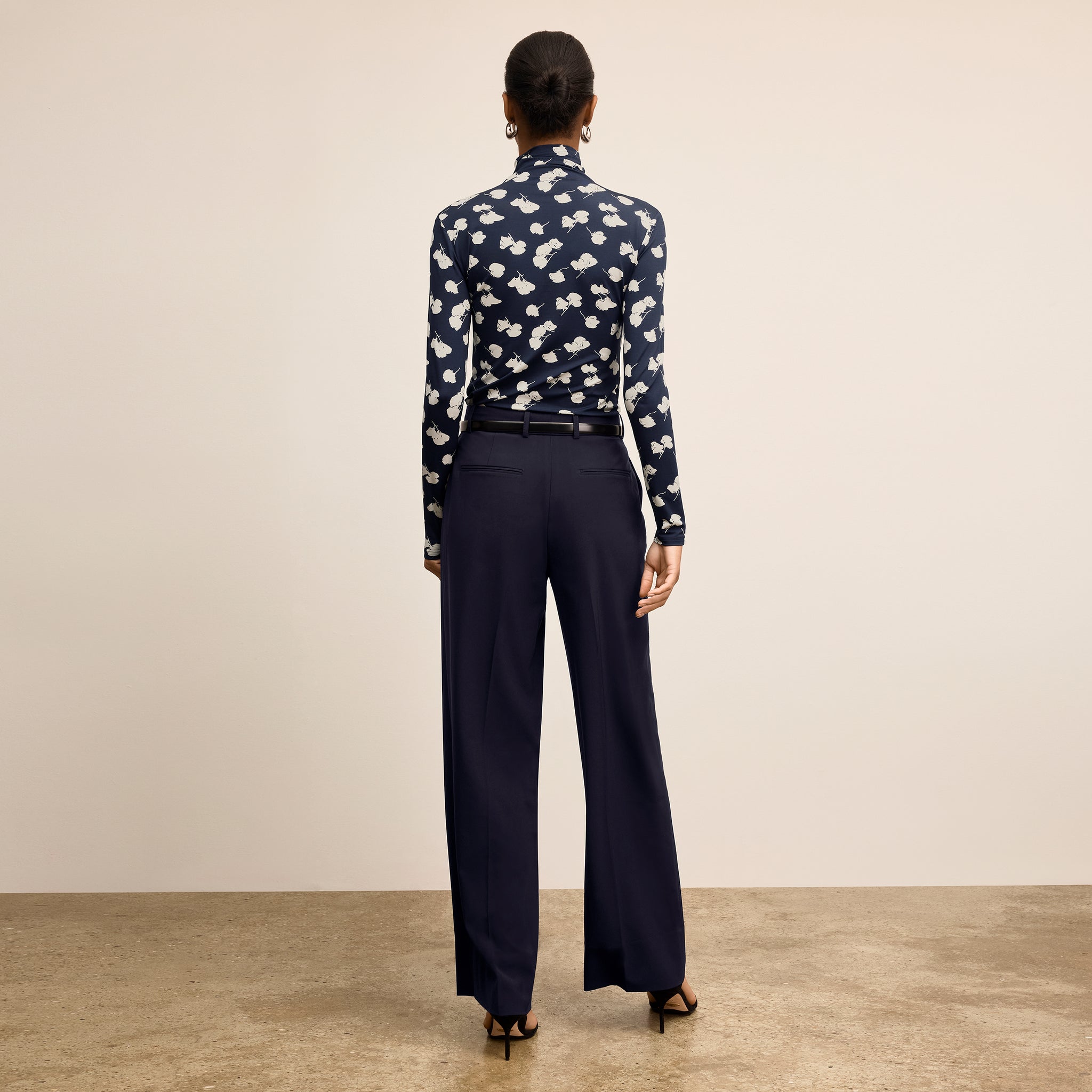 Person wearing a navy patterned blouse and dark pants on a beige background