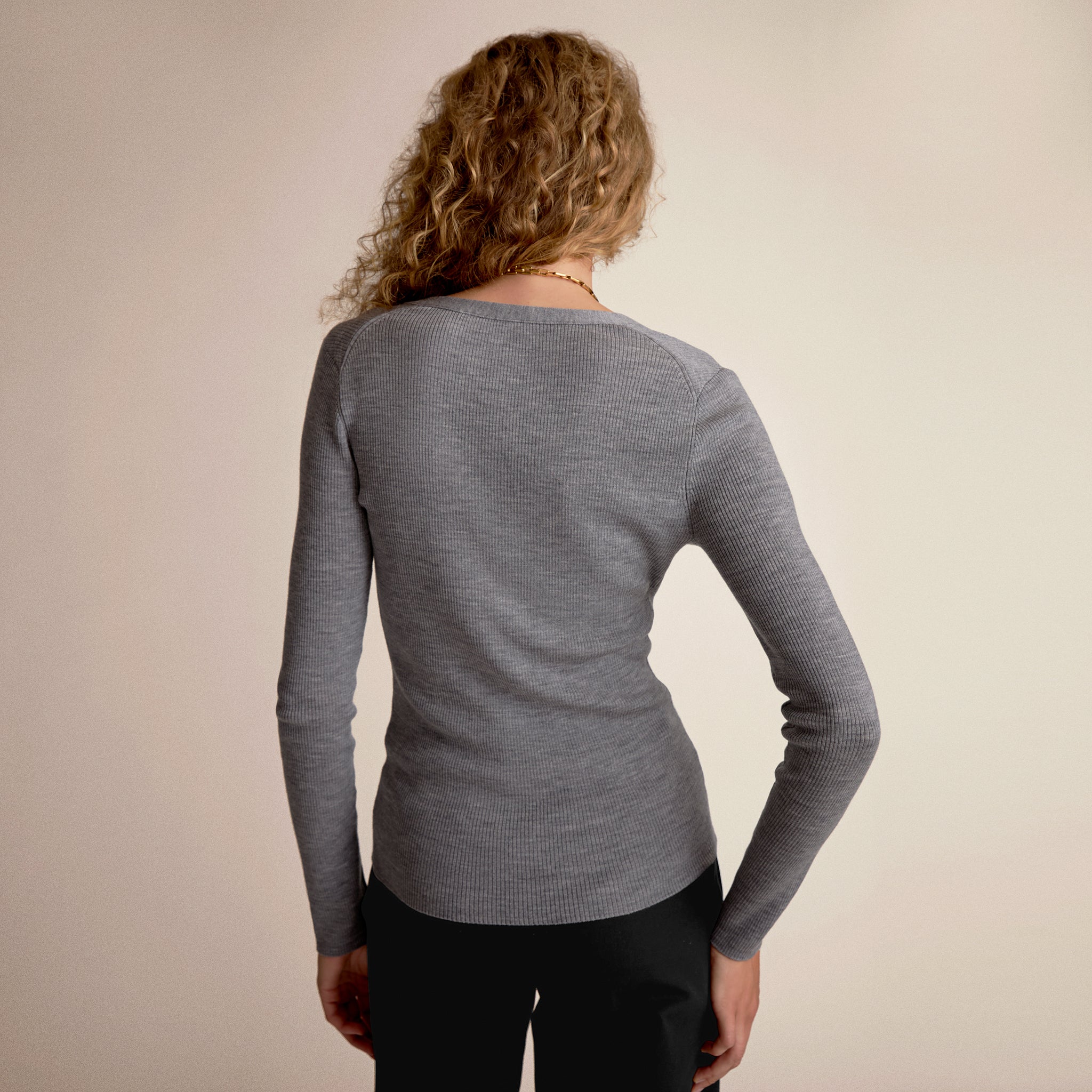 Person wearing a gray long-sleeve shirt against a beige background