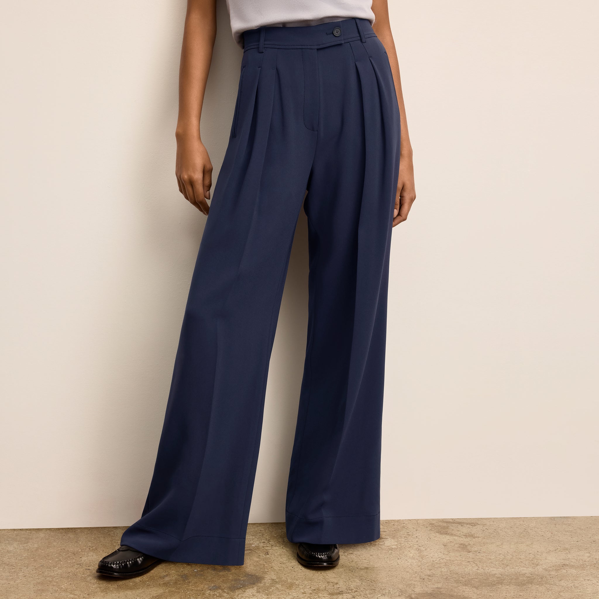 Navy wide-leg pants worn by a woman against a beige wall. 