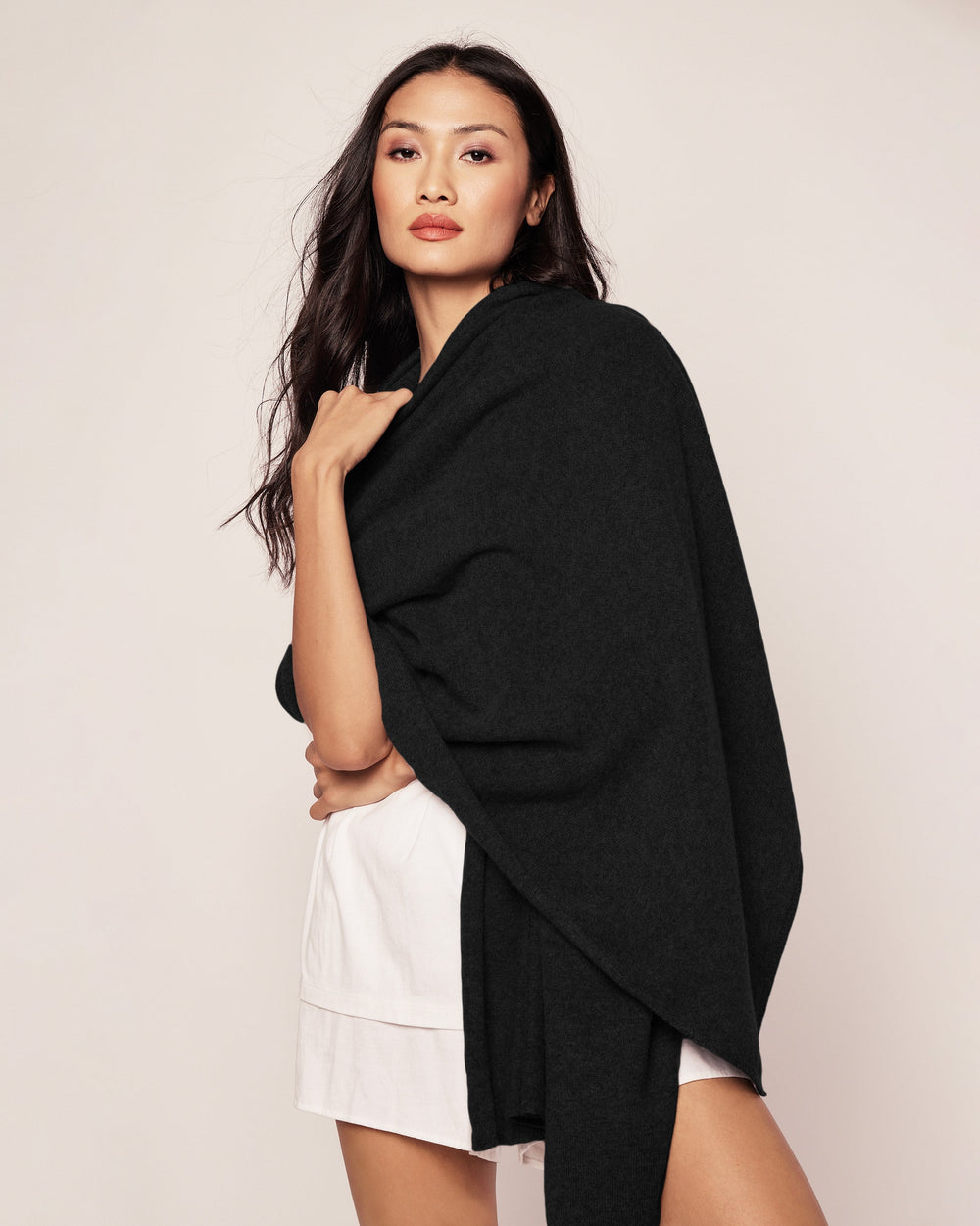 Woman wearing a black shawl over a white outfit against a plain background
