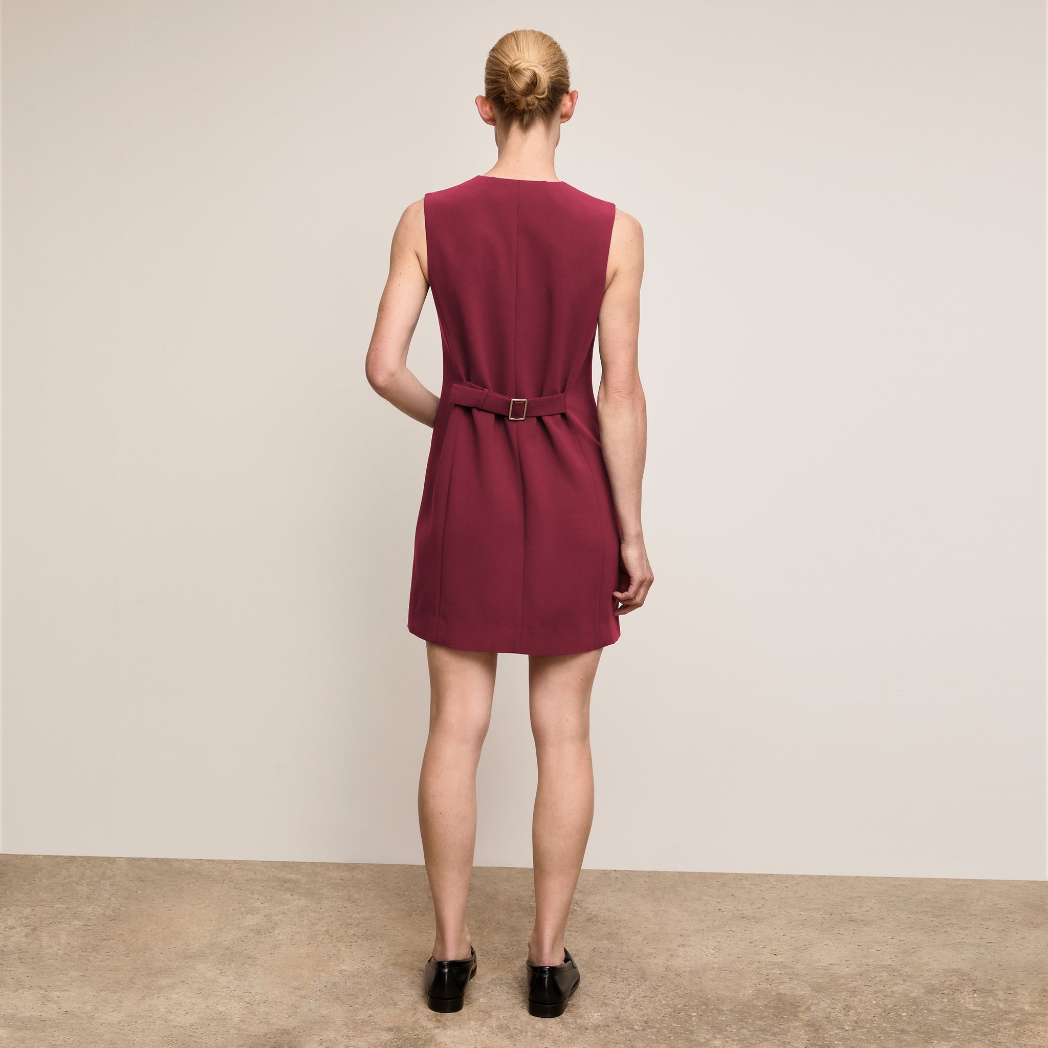 Woman wearing a burgundy dress with a belt on a plain background