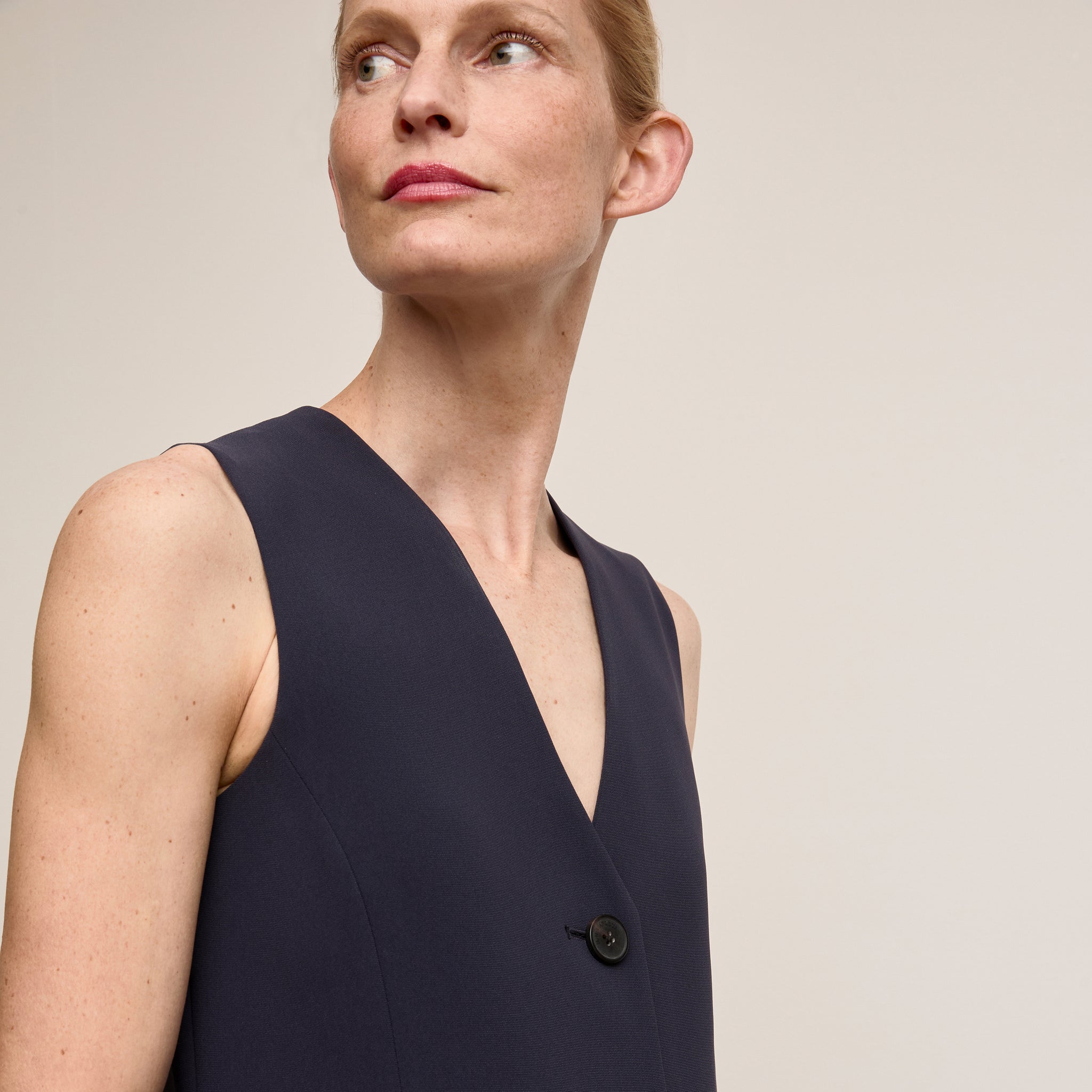 Woman wearing a navy blue sleeveless top against a beige background