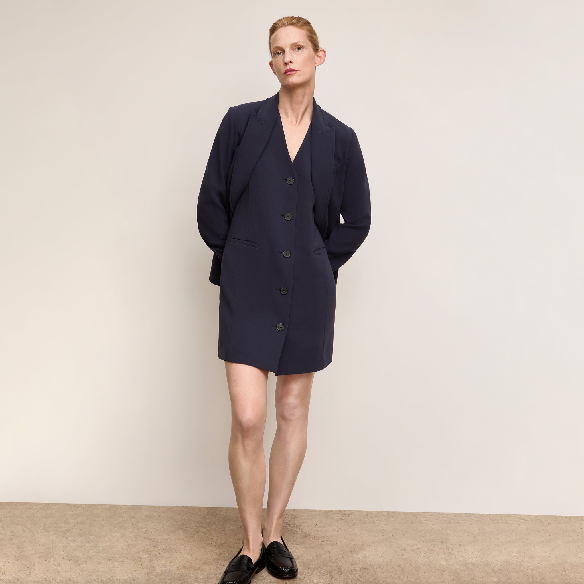 Woman wearing a navy blue blazer dress against a plain background