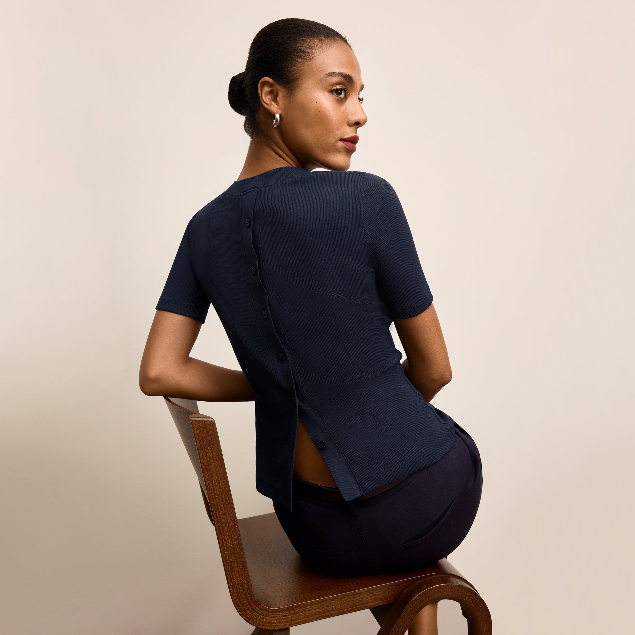 Woman sitting on a wooden chair wearing a navy blue outfit against a beige background
