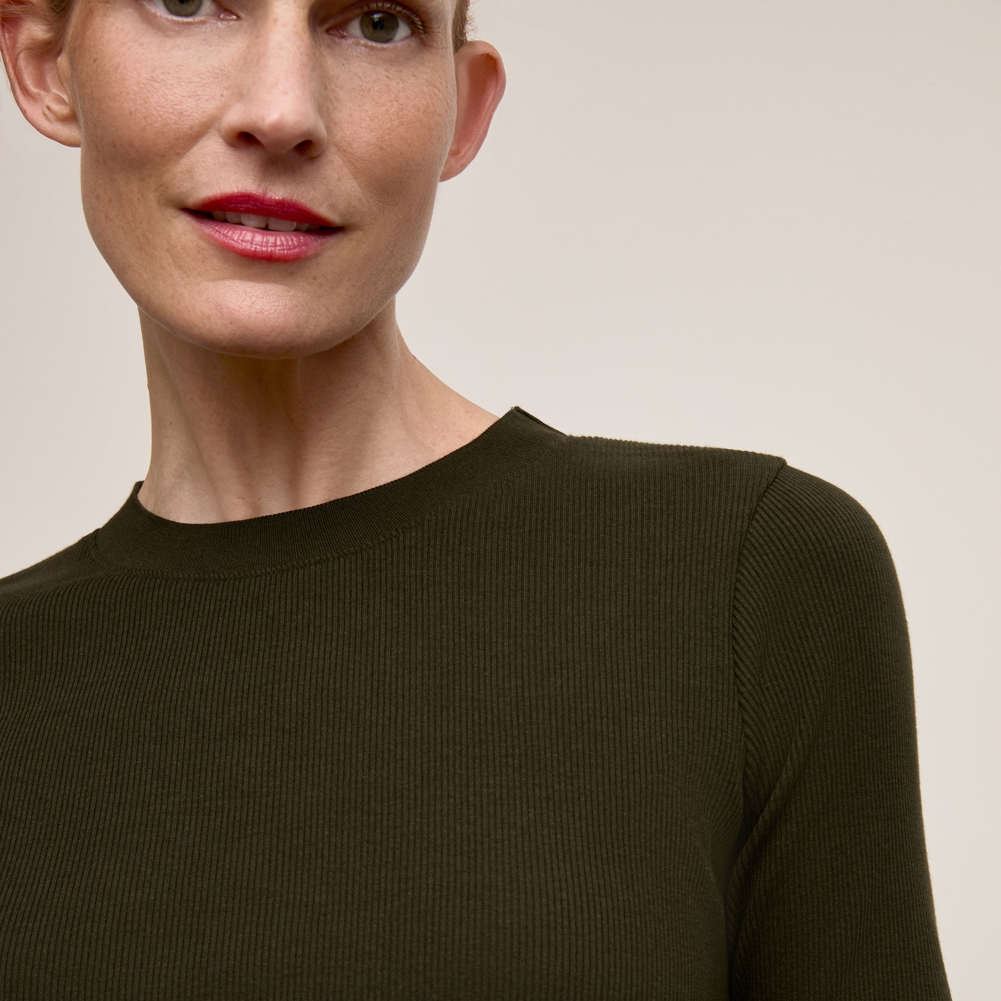 Woman wearing a dark green sweater against a beige background