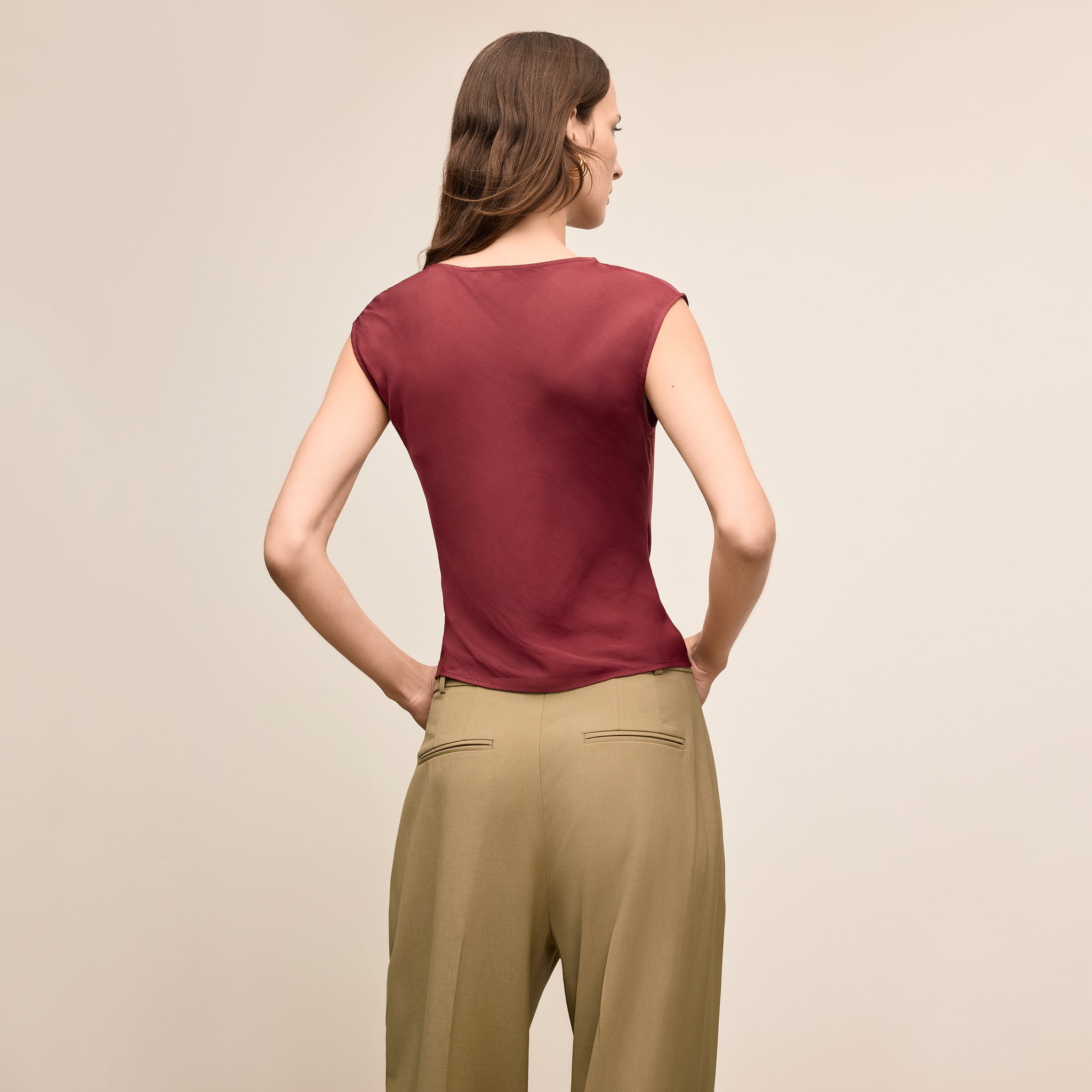 Woman wearing a burgundy top and beige pants against a beige background