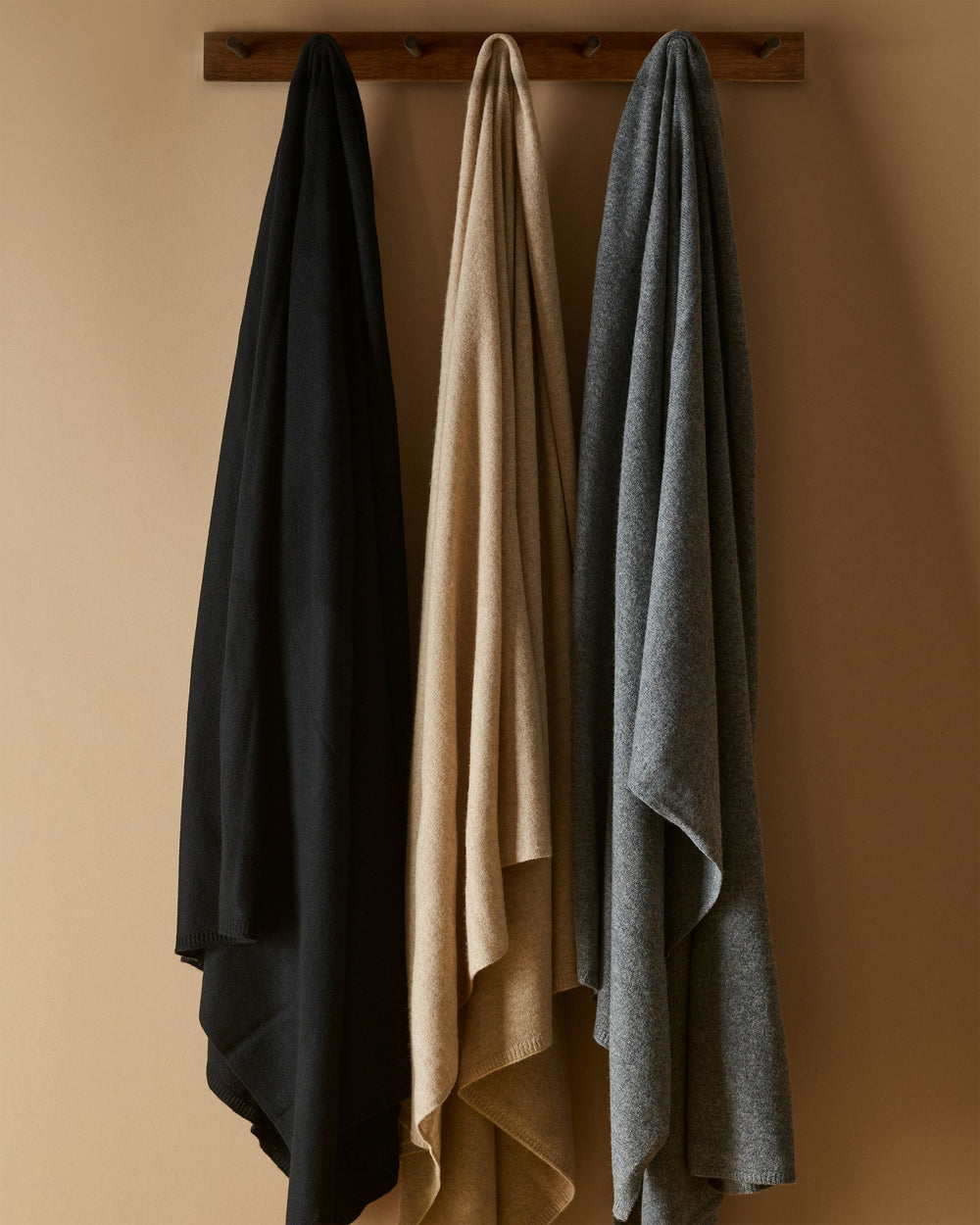 Three shall in black, beige, and gray hanging on a wooden rack against a beige wall.