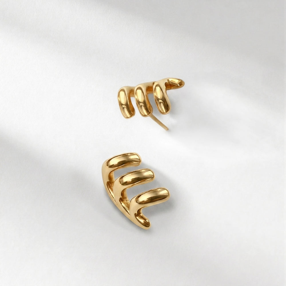 A pair of gold-plated spiral claw earrings on a soft, light gray fabric background.