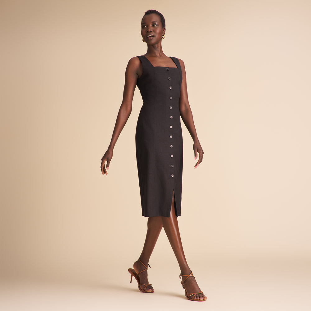 Woman wearing a black linen dress with black buttons on a beige background