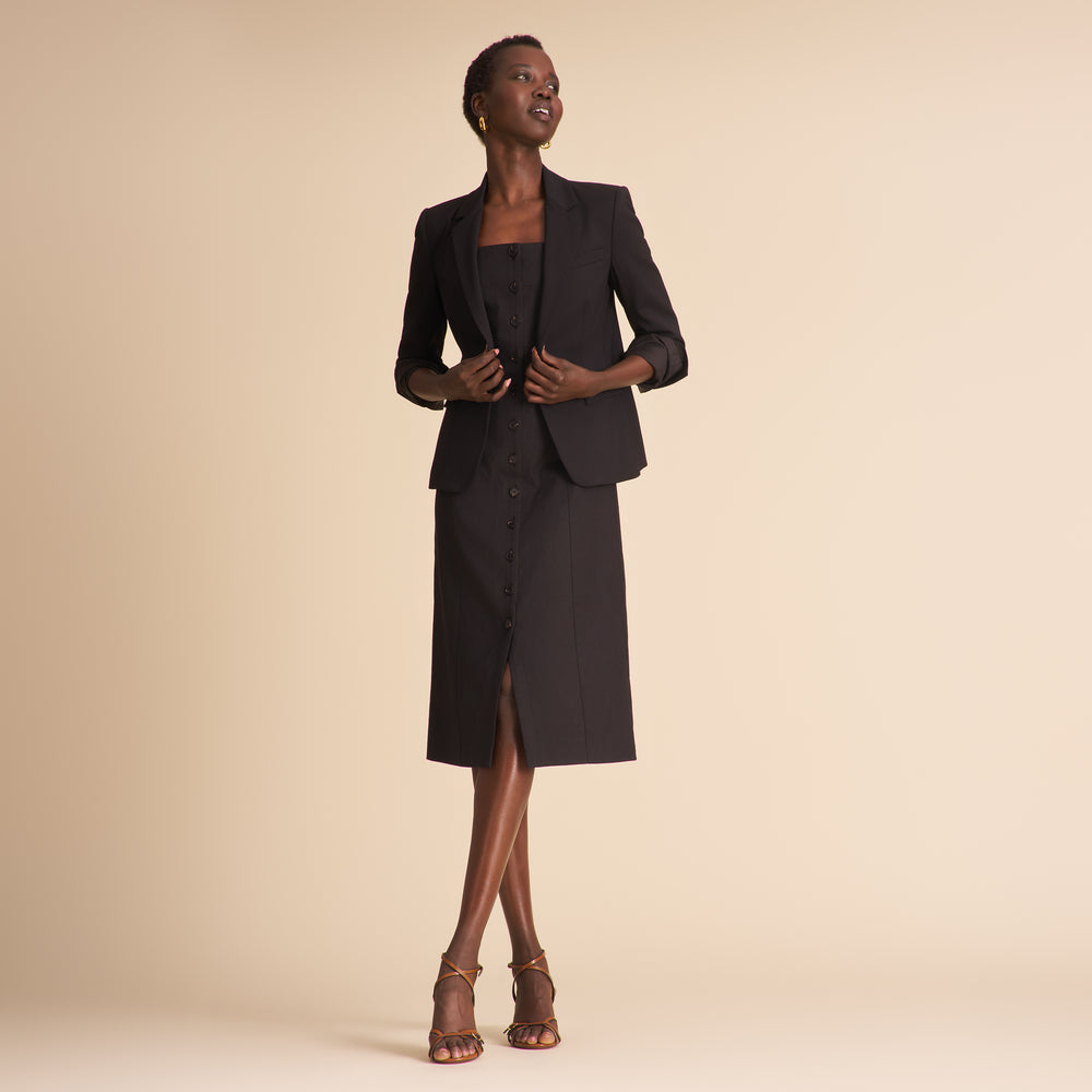 Woman wearing a black linen dress with black buttons on a beige background