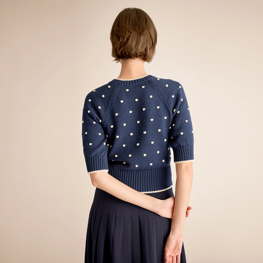 Person wearing a navy blue sweater with white polka dots on a beige background