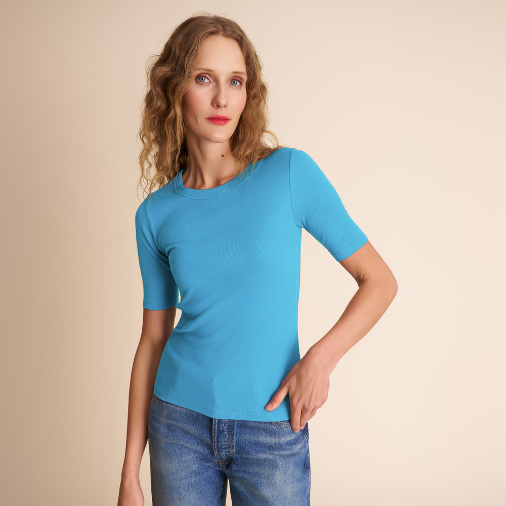 Woman wearing a blue t-shirt and jeans against a beige background