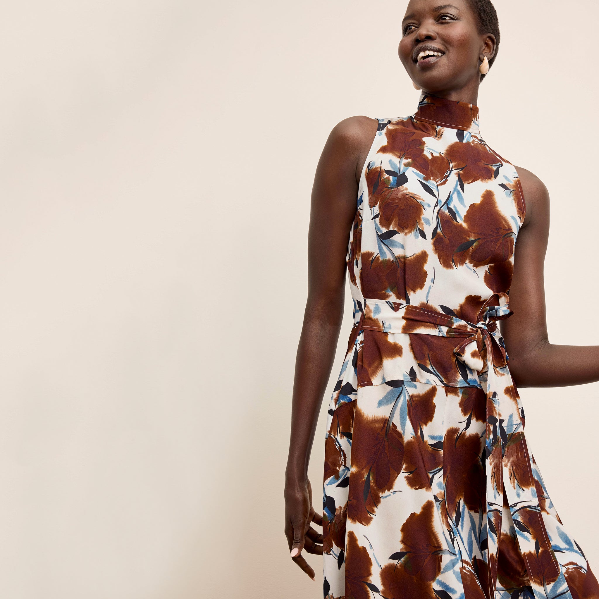 Woman wearing a sleeveless dress with a brown and white abstract pattern on a beige background