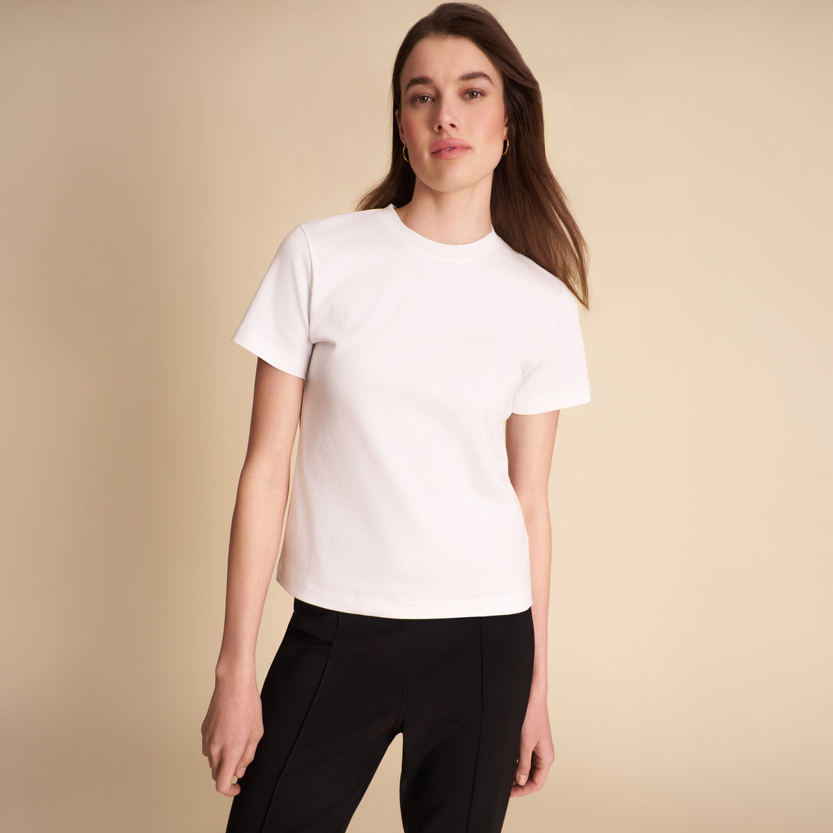 Woman wearing a white t-shirt and black pants against a beige background