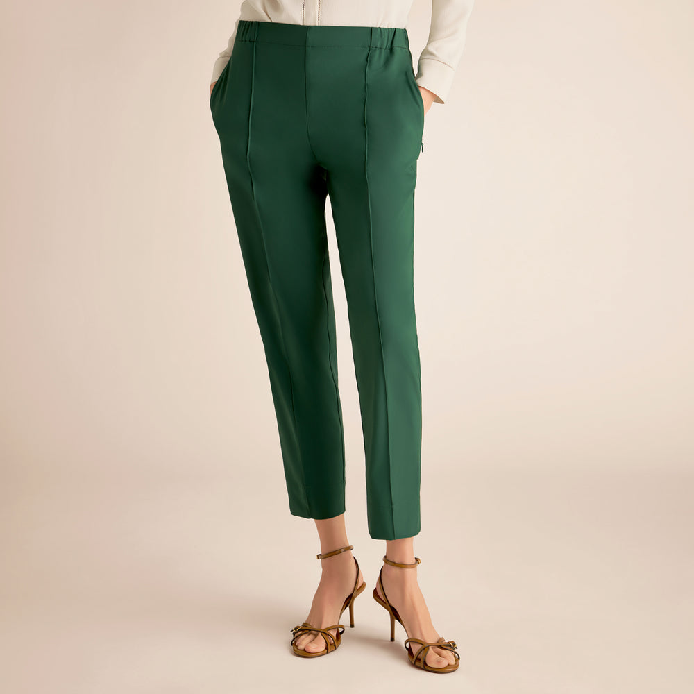 Green pants worn with a white top and gold sandals on a beige background