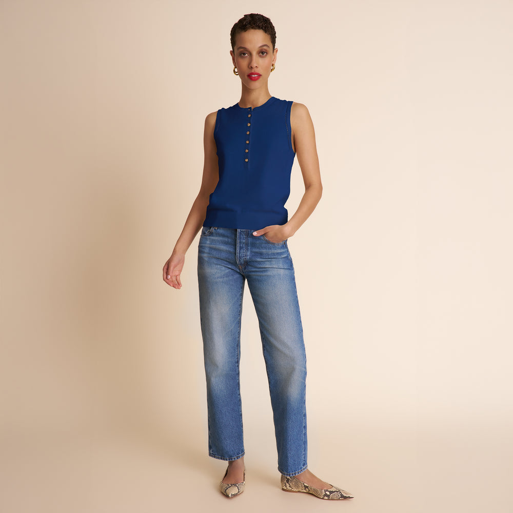 Woman wearing a blue sleeveless top and jeans on a beige background