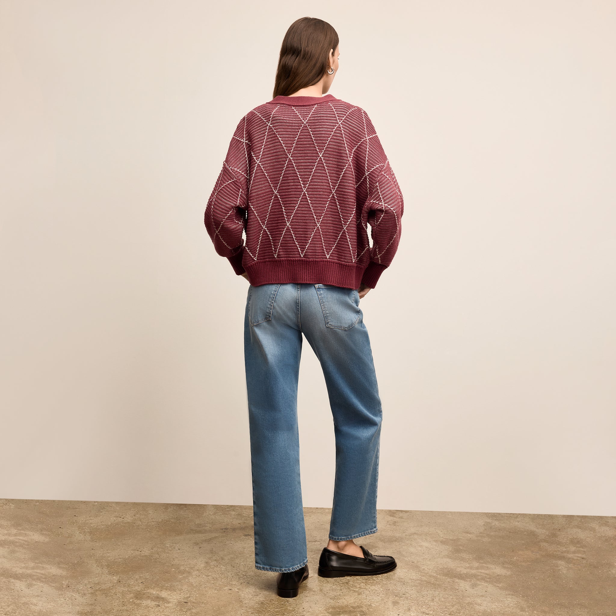 Person wearing a patterned sweater and blue jeans standing against a plain background