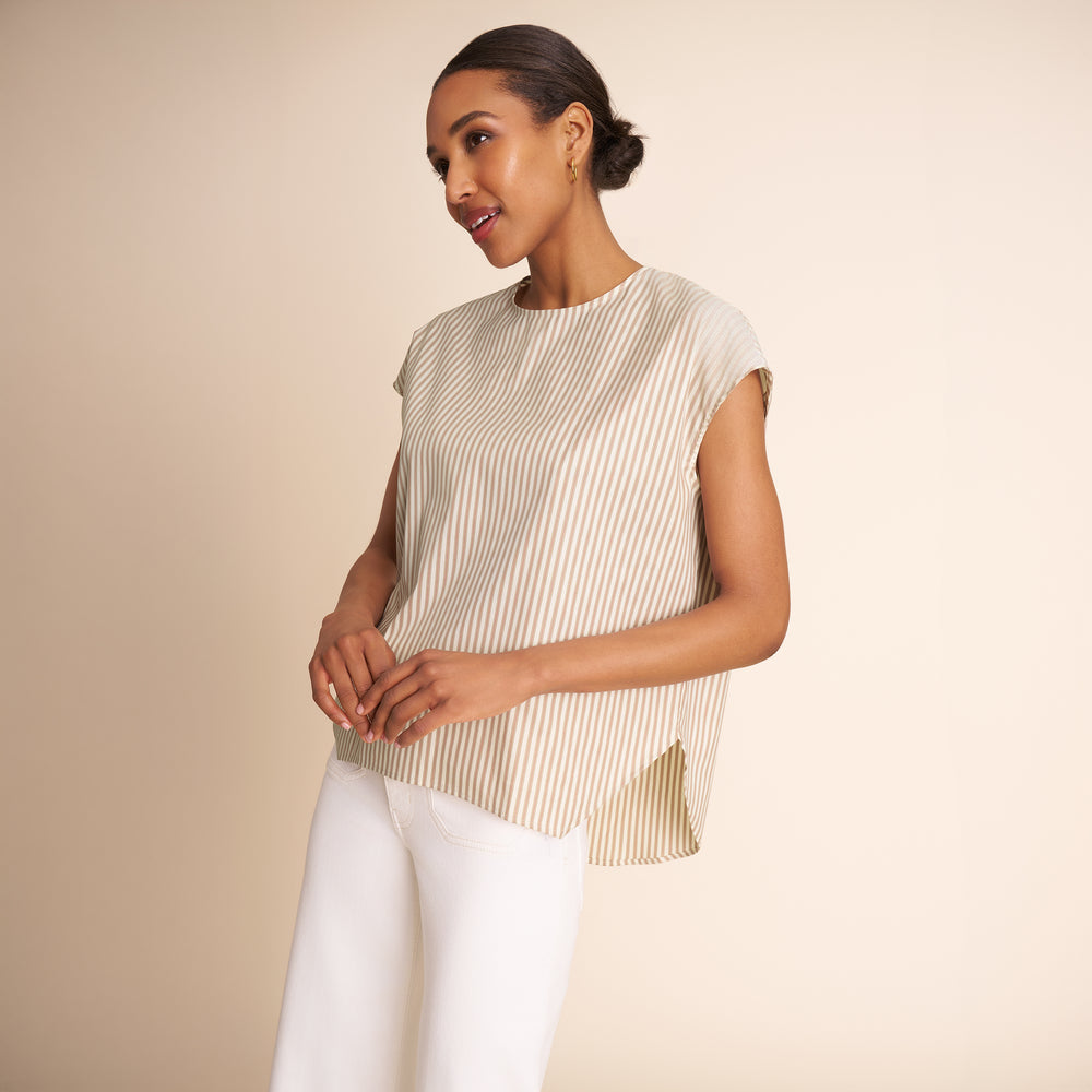 Woman wearing a sleeveless striped top and white pants against a beige background