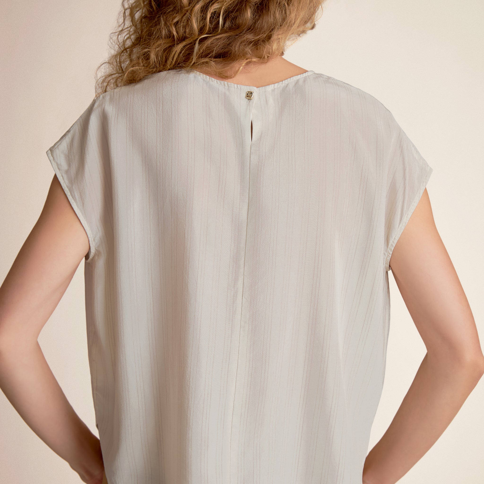 Light gray blouse worn by a person on a beige background