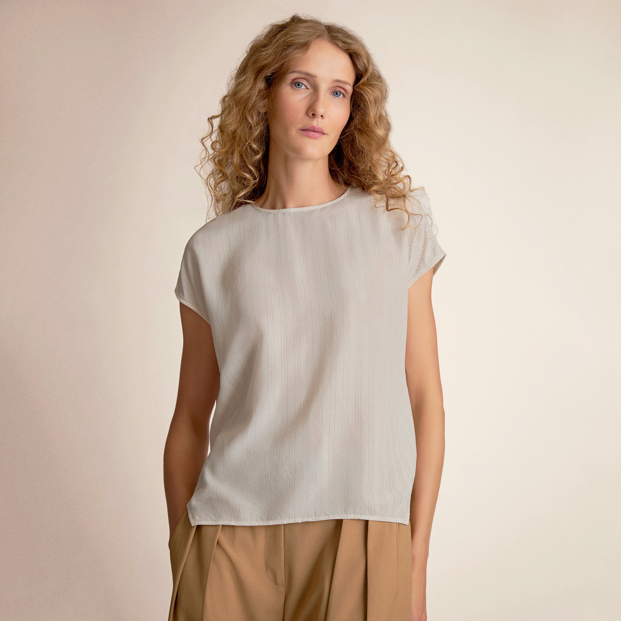 Woman wearing a light-colored top and beige pants against a plain background 
