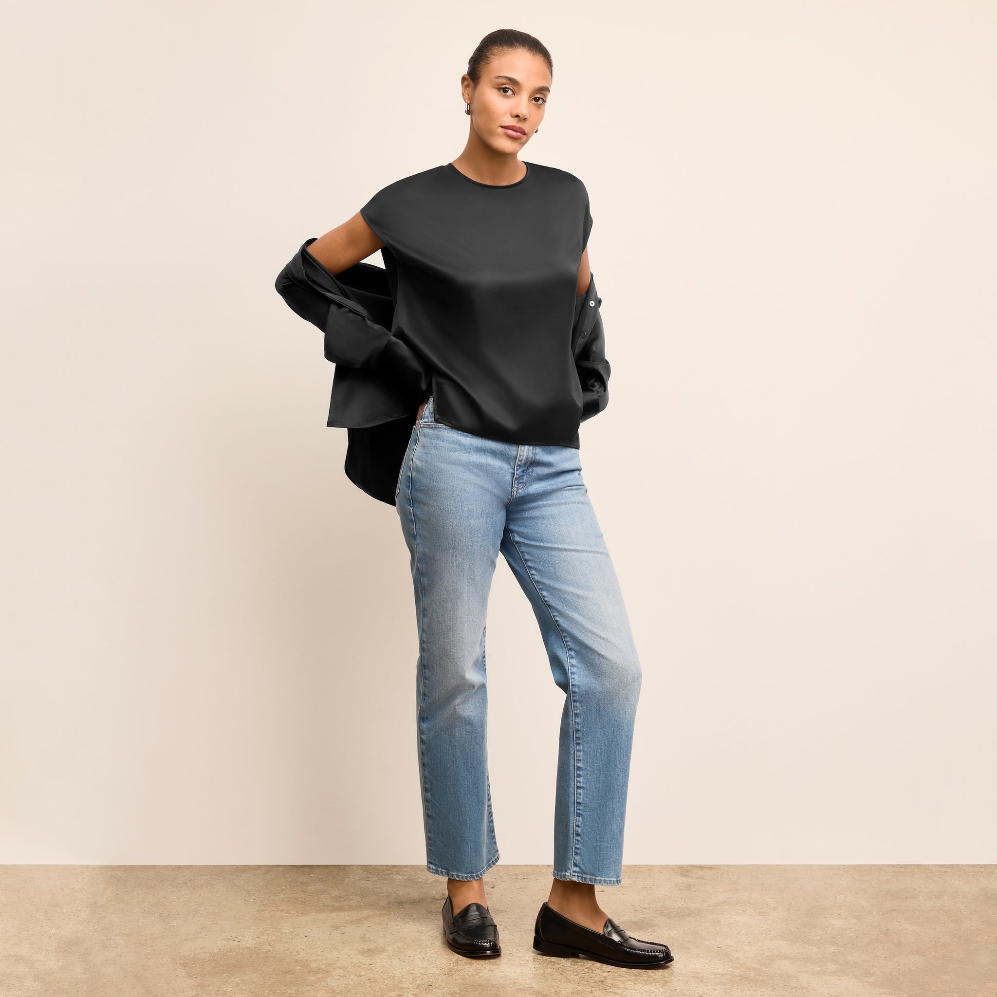 Woman wearing a black top and blue jeans against a beige background