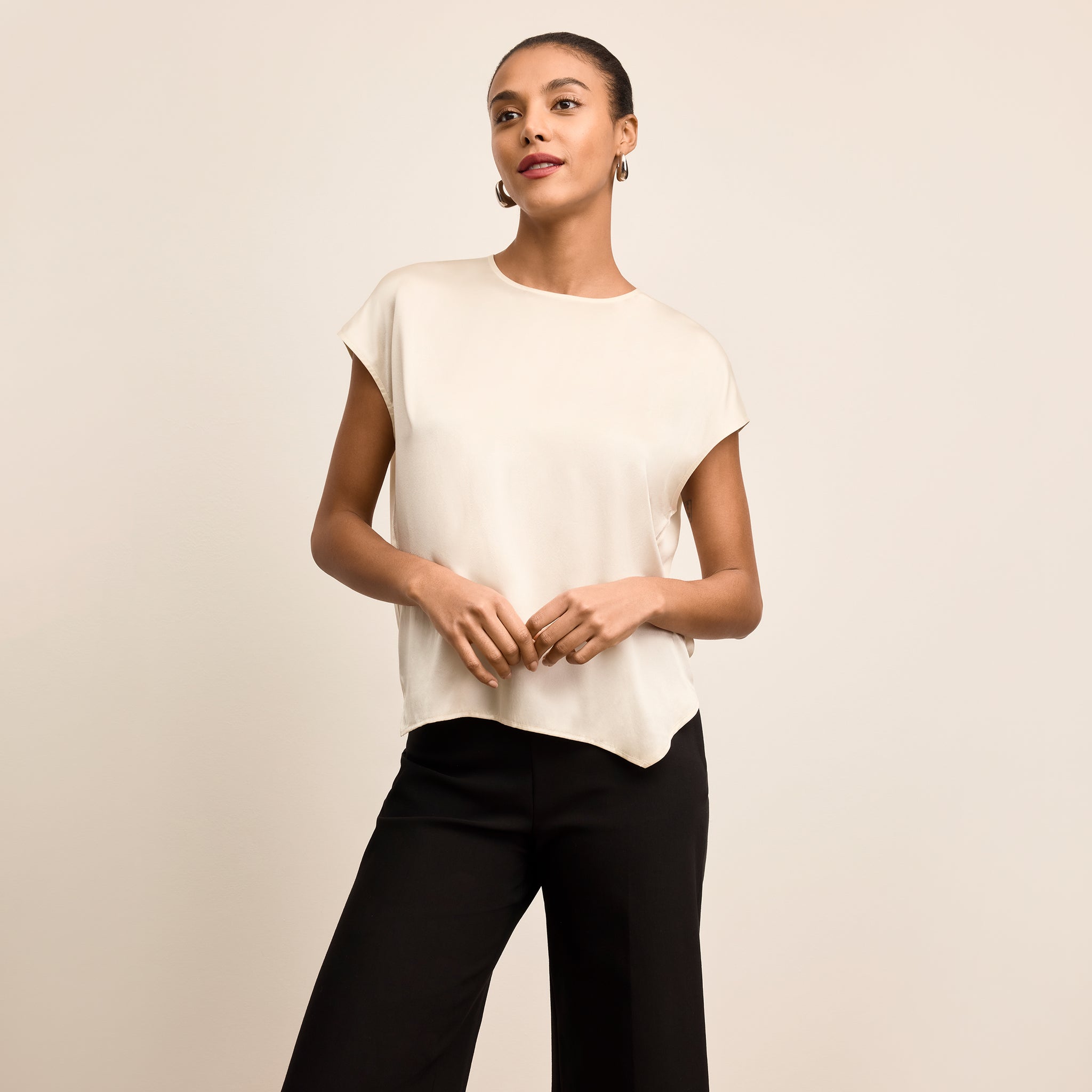 Woman wearing a white blouse and black pants against a beige background 