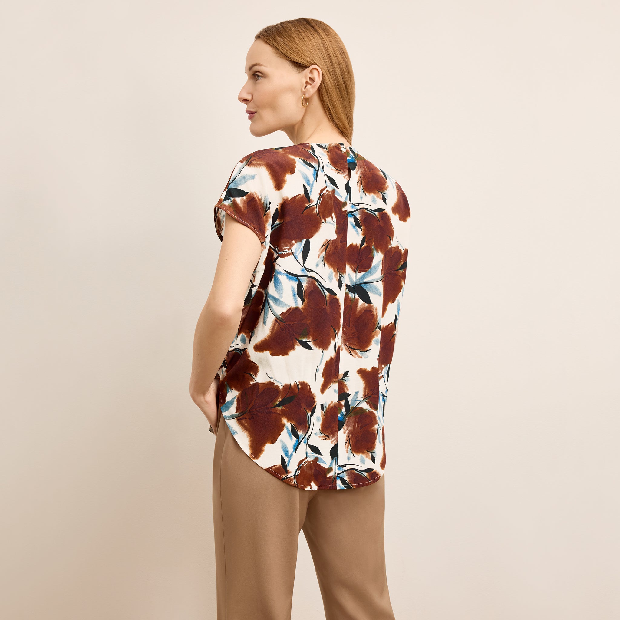 Woman wearing a floral blouse with brown and white pattern on a beige background