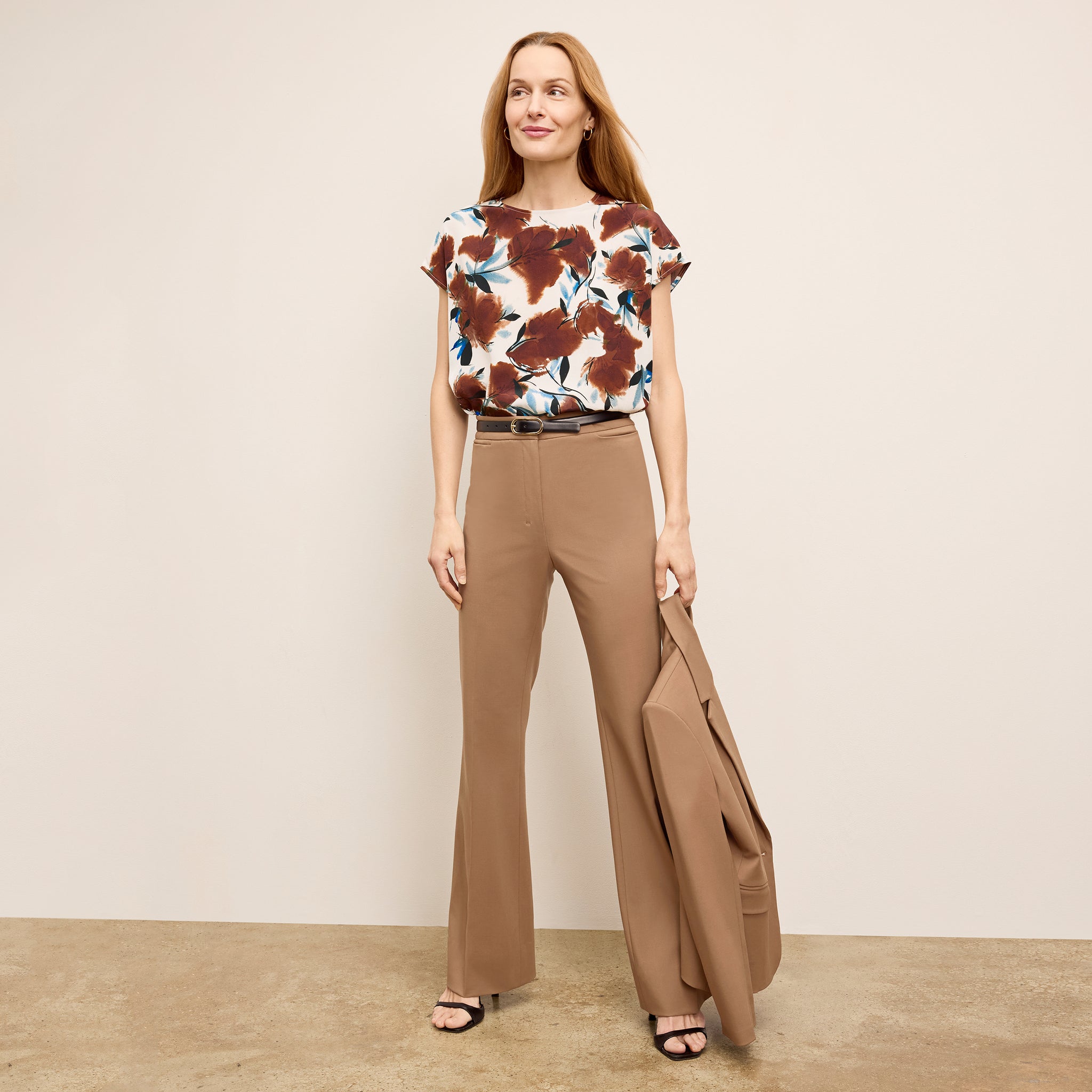 Woman wearing a patterned top and brown pants with a beige background
