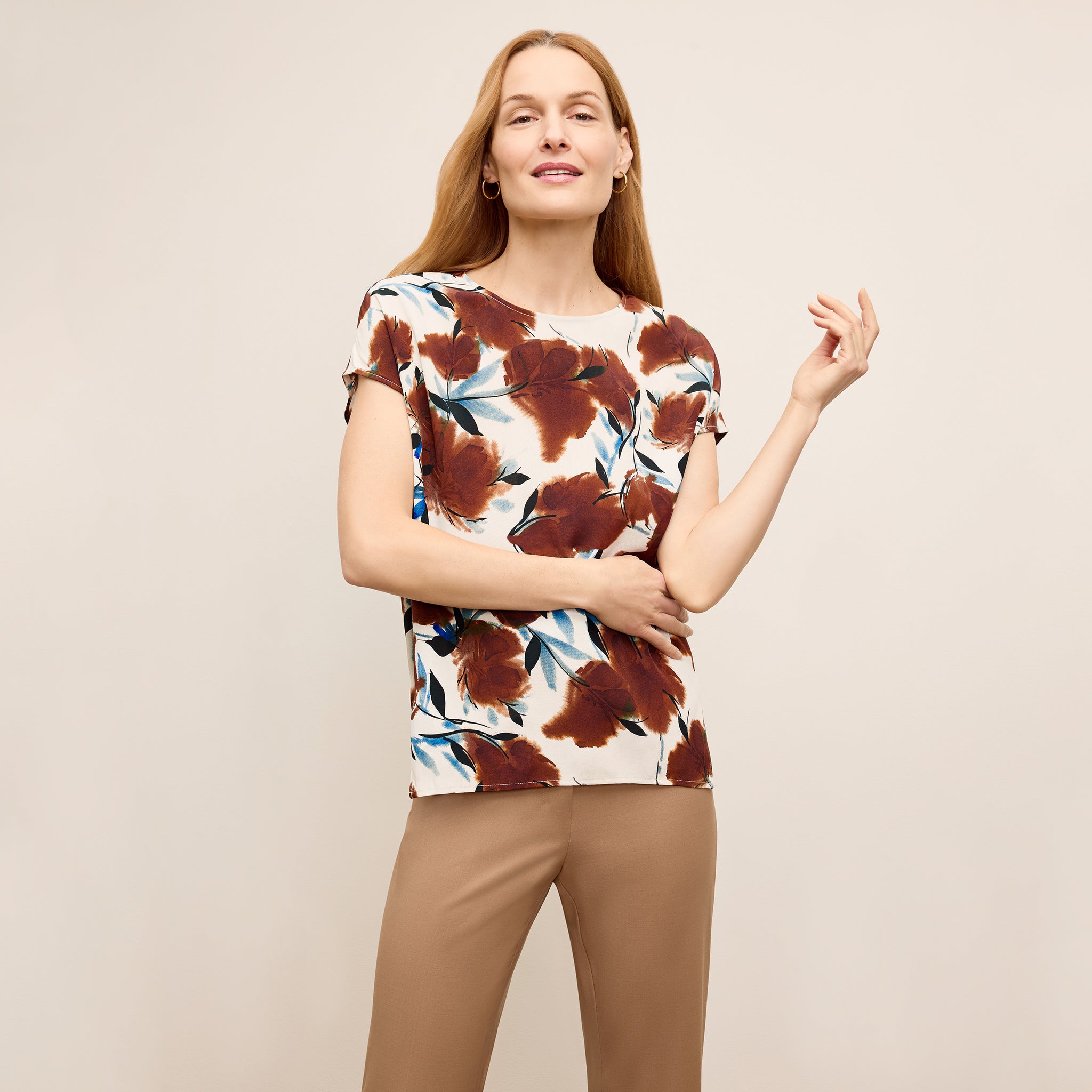 Woman wearing a floral top and beige pants against a beige background 