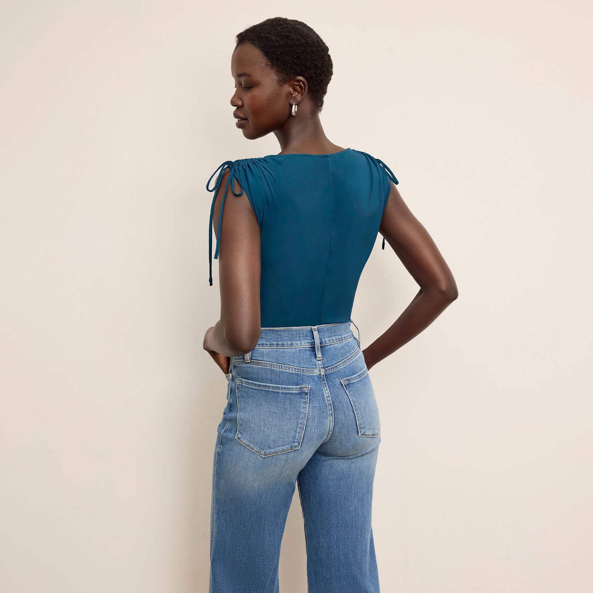 Woman wearing a teal top and blue jeans against a beige background