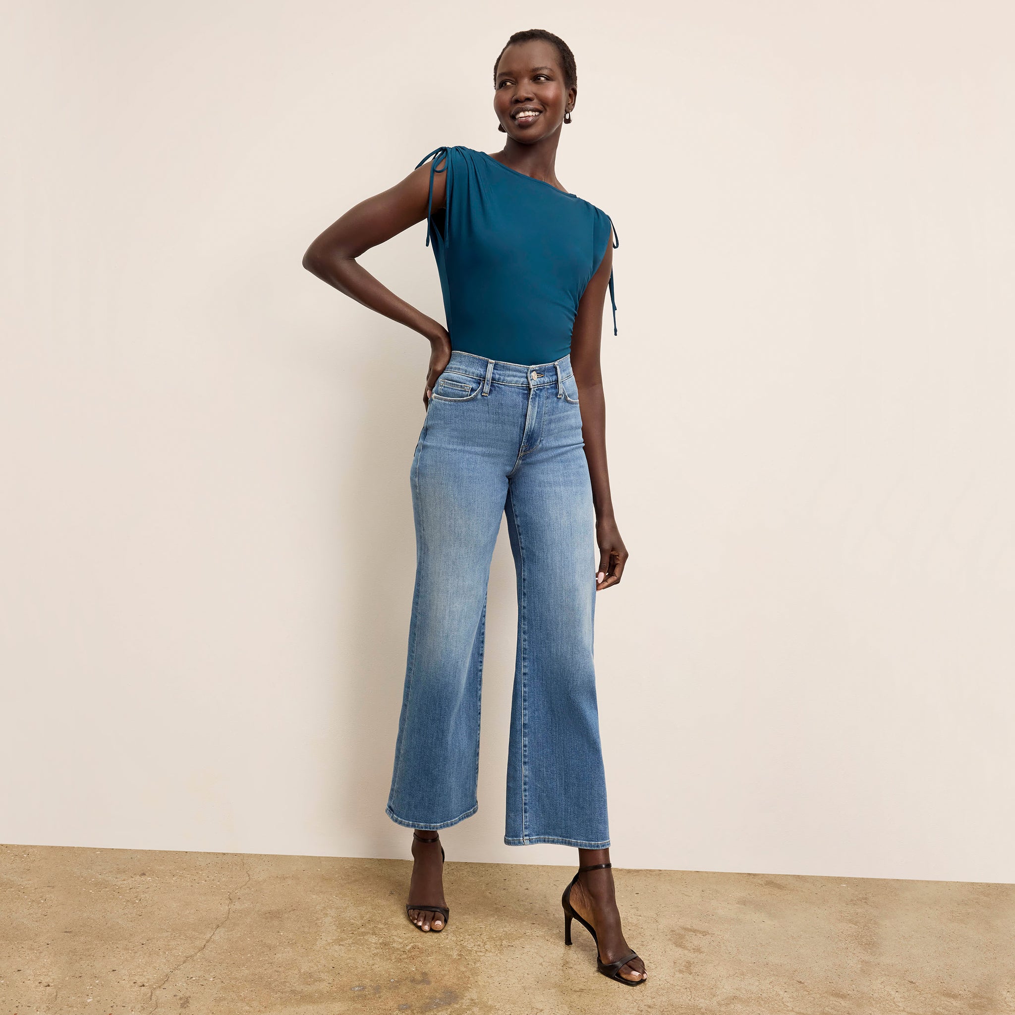 Woman wearing a teal top and blue jeans against a beige background