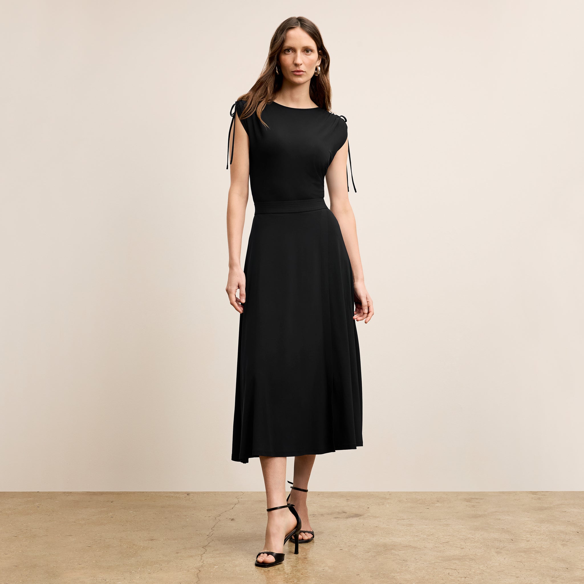 Woman wearing a black dress with sheer sleeves against a beige background