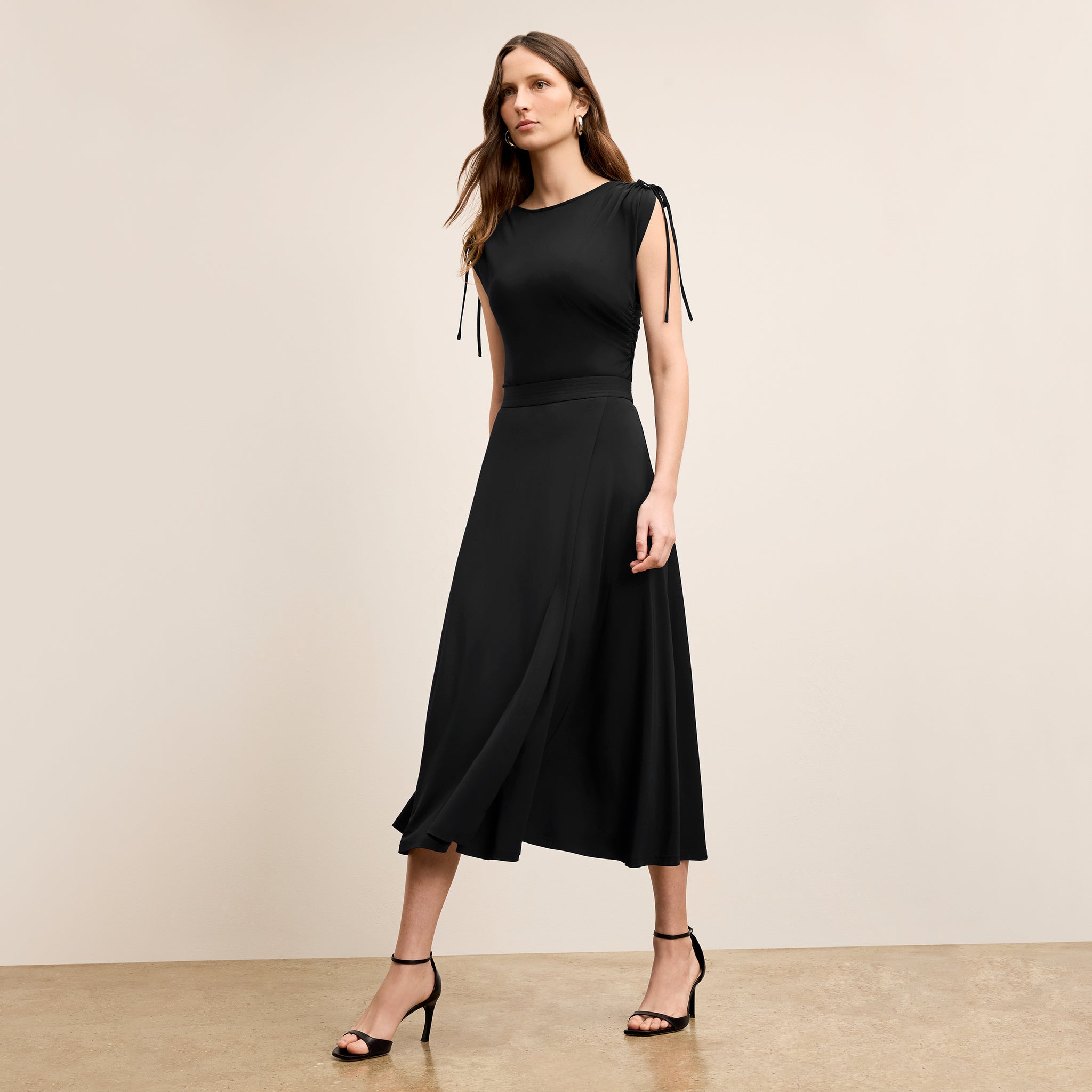 Woman wearing a black dress with tie sleeves against a beige background