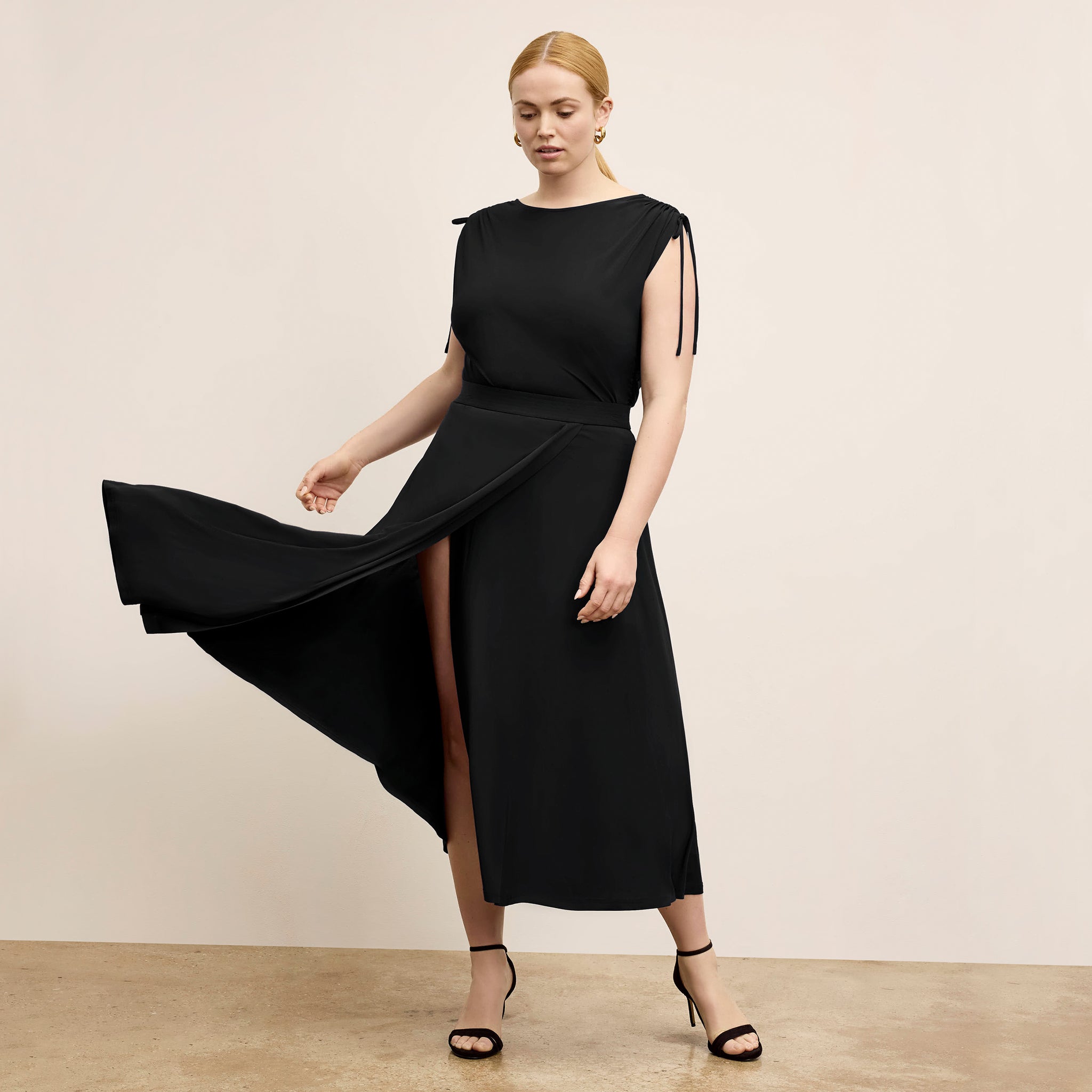 Woman wearing a black dress with a slit on a beige background