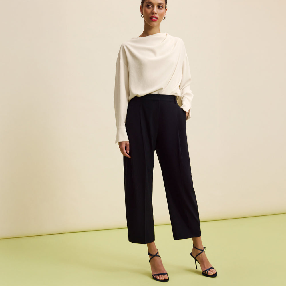 Woman wearing a white blouse and black pants against a plain background