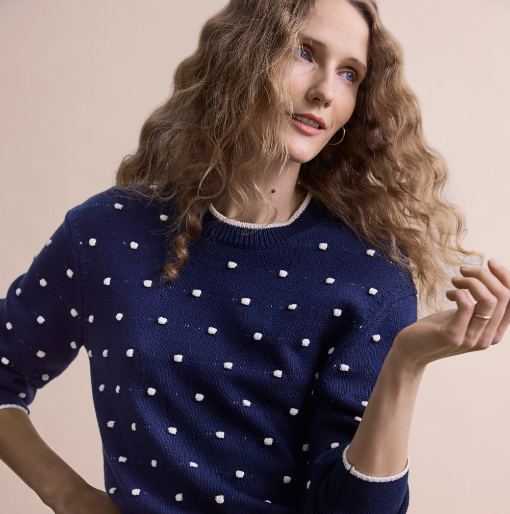 Person wearing a navy blue sweater with white polka dots on a beige background