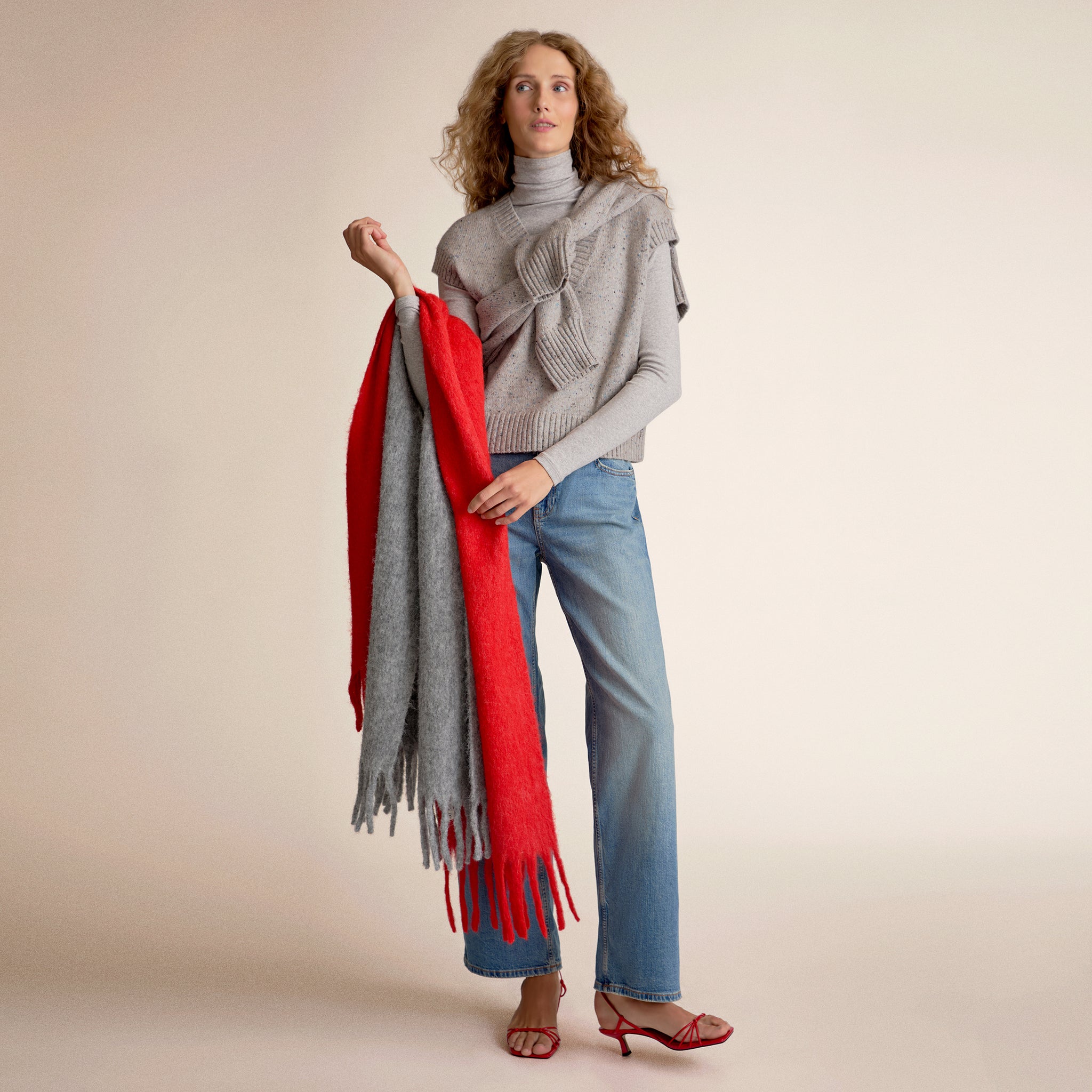 Woman wearing a gray sweater vest holding two scarves