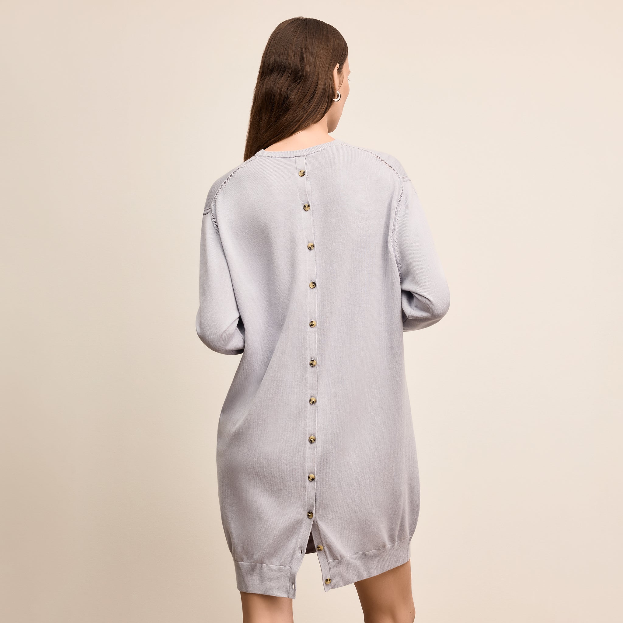 Woman wearing a light gray dress with buttons on a beige background