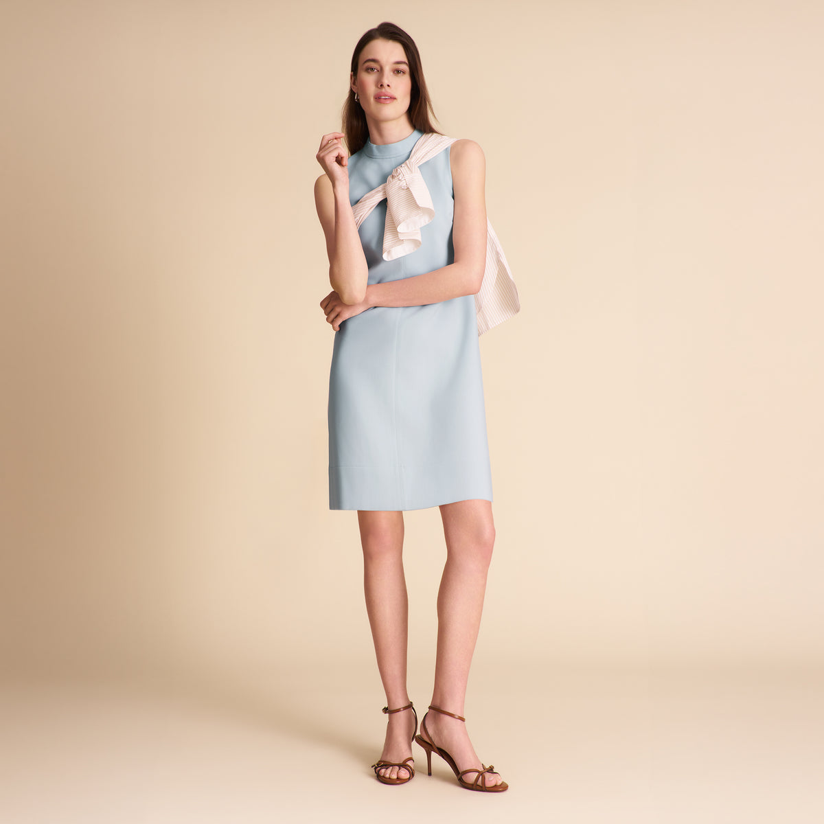 Woman wearing a light blue dress with an ivory sweater on a beige background