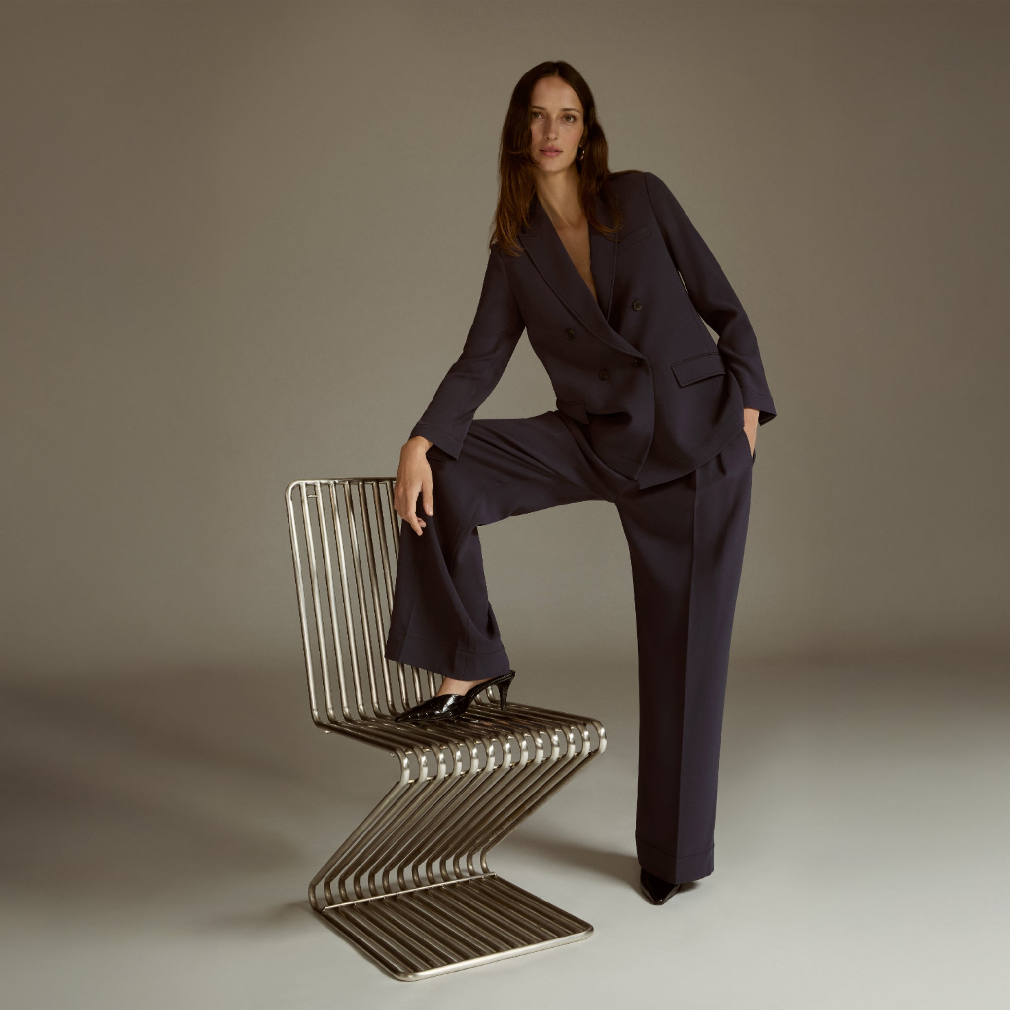 Woman in a dark suit sitting on a modern chair against a plain background