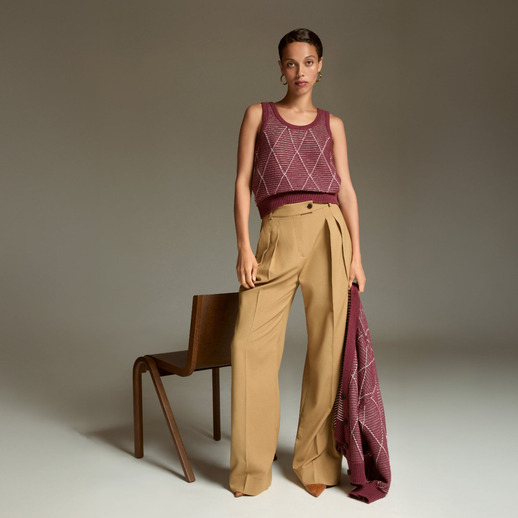 Woman wearing a patterned sleeveless top and beige pants, holding a matching fabric, against a neutral background.