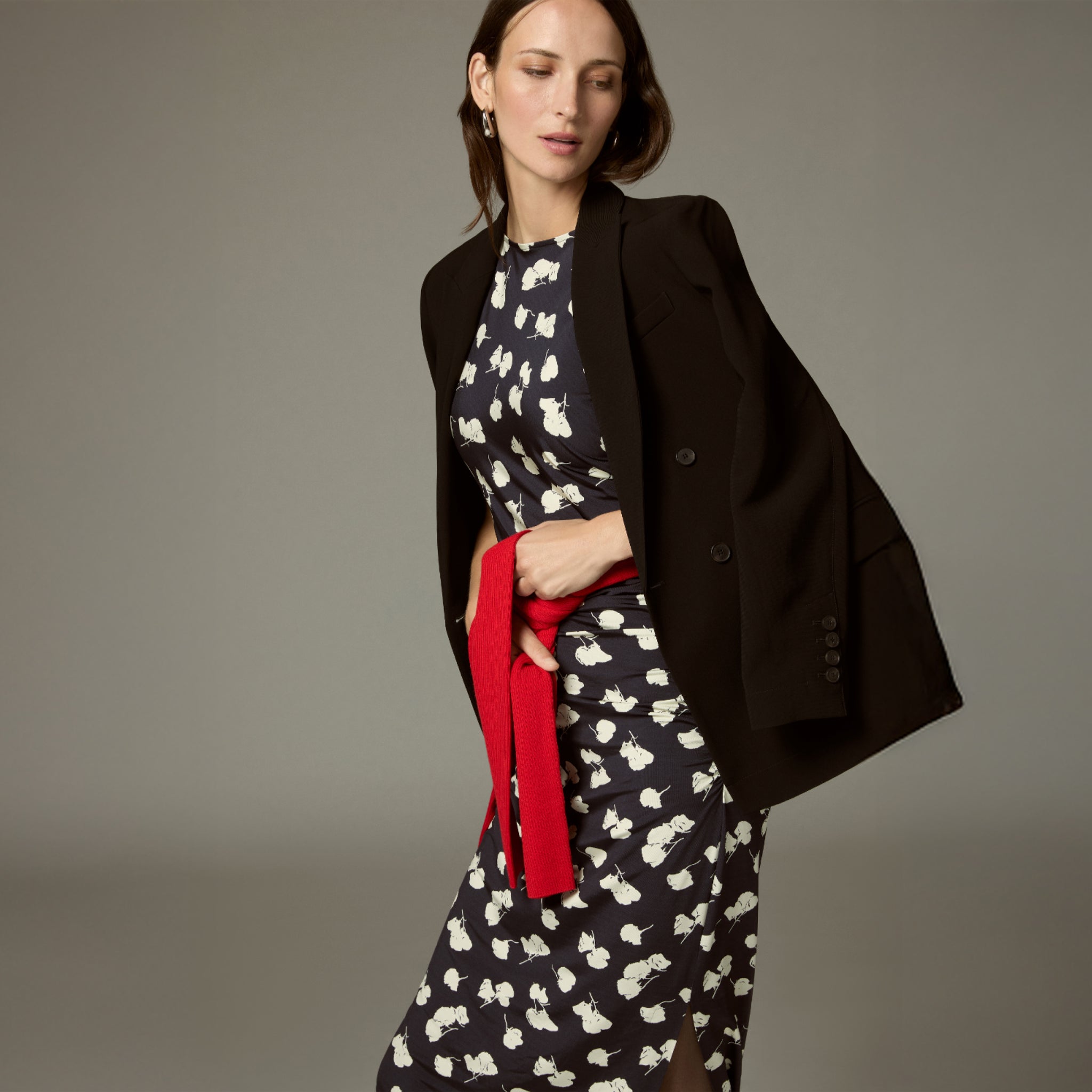 Woman wearing a black coat over a patterned dress with a red belt against a neutral background